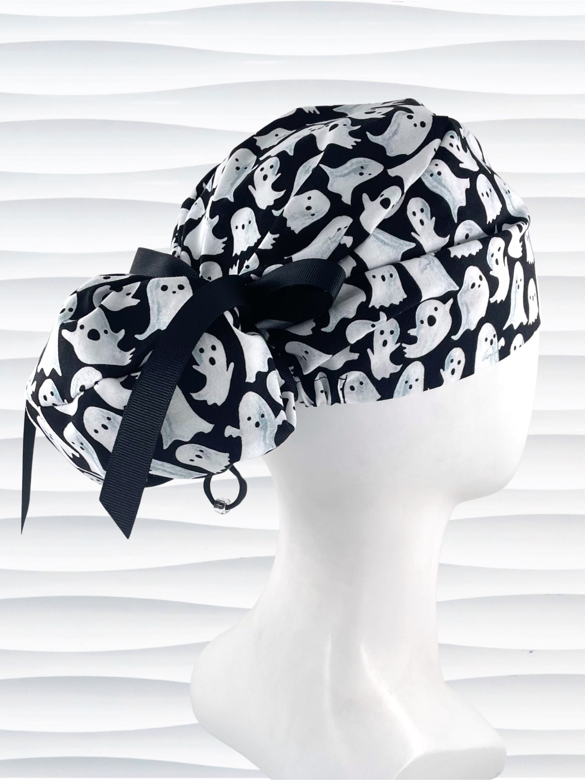 Euro Pony style surgical ponytail scrub cap with friendly white ghosts tossed all over black cotton fabric and finished with grosgrain ribbon ties.
