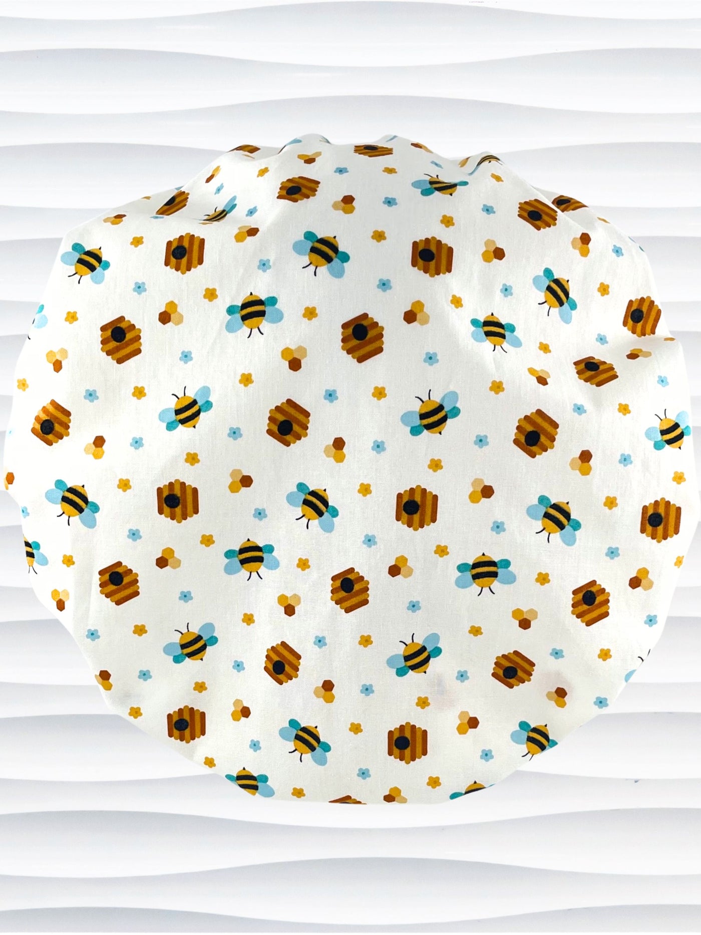 Bouffant style surgical scrub cap with an allover print of bumble bees, beehives, honeycombs, and flowers on white cotton fabric 