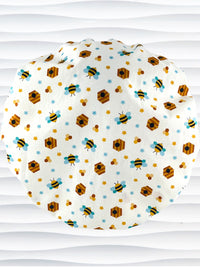 Bouffant style surgical scrub cap with an allover print of bumble bees, beehives, honeycombs, and flowers on white cotton fabric 