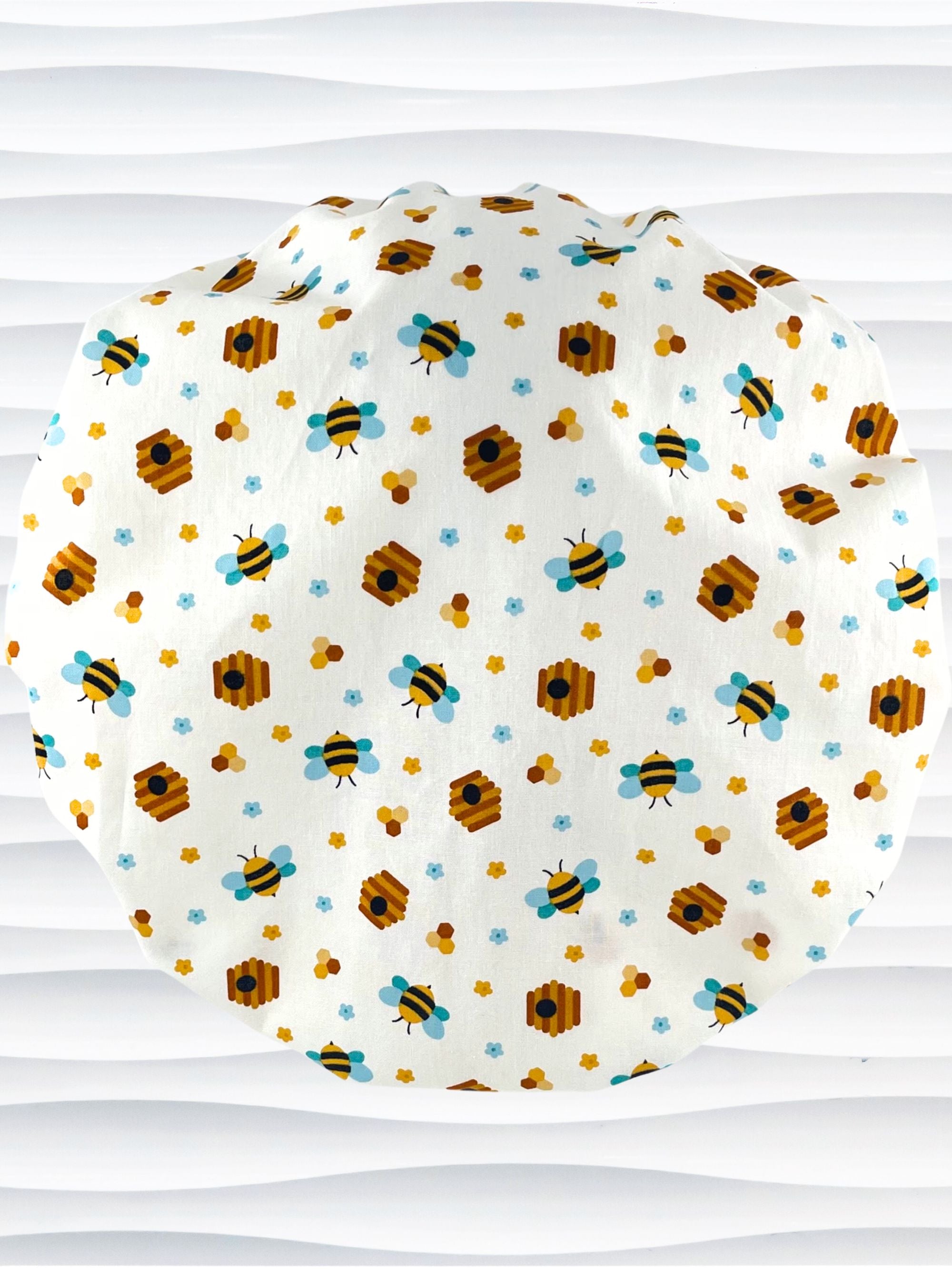 Bouffant style surgical scrub cap with an allover print of bumble bees, beehives, honeycombs, and flowers on white cotton fabric 