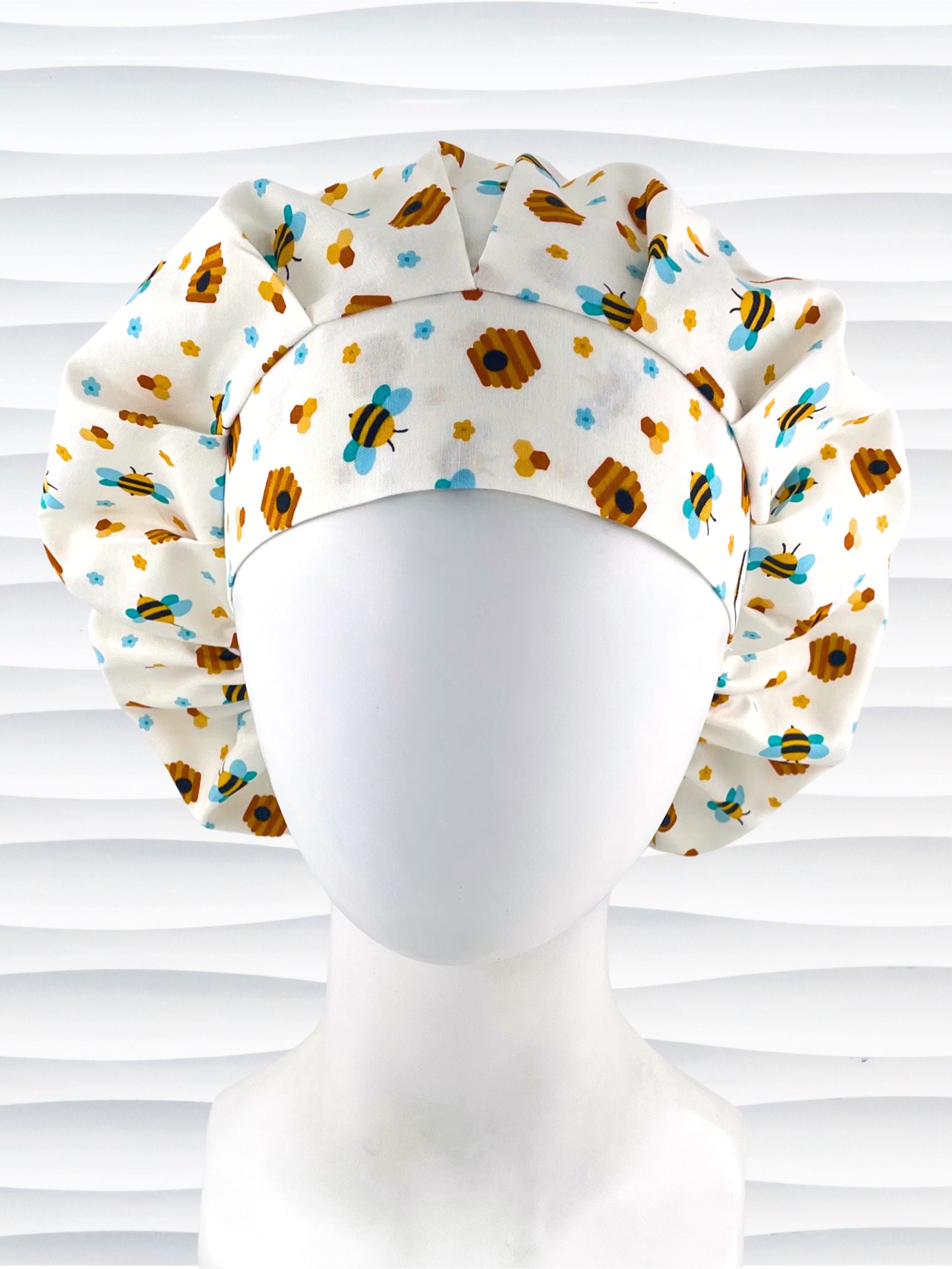 Bouffant style surgical scrub cap with an allover print of bumble bees, beehives, honeycombs, and flowers on white cotton fabric 