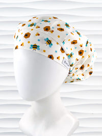 Bouffant style surgical scrub cap with an allover print of bumble bees, beehives, honeycombs, and flowers on white cotton fabric 