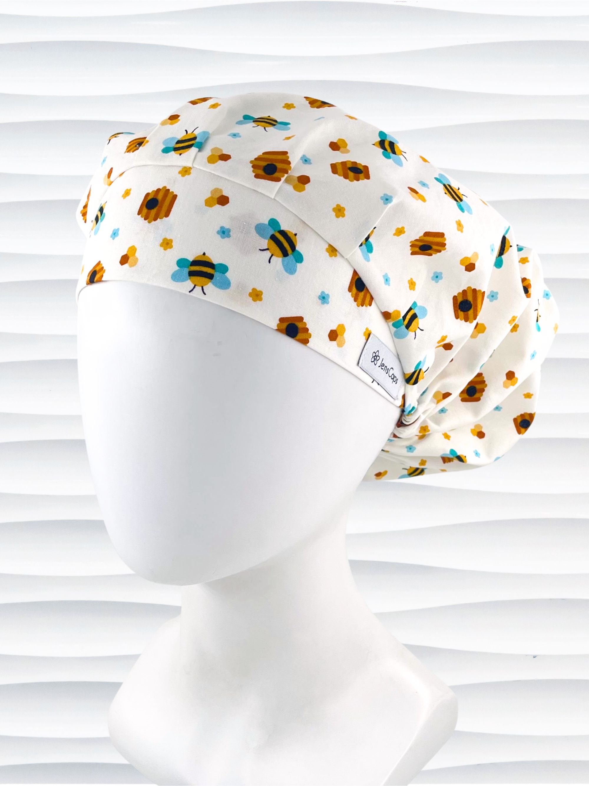 Bouffant style surgical scrub cap with an allover print of bumble bees, beehives, honeycombs, and flowers on white cotton fabric 