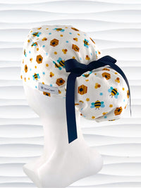 Ponytail style surgical scrub cap with honey bees with blue wings, blue and yellow daisies, and bee hives scattered all over this cotton fabric and tied with a grosgrain ribbon.
