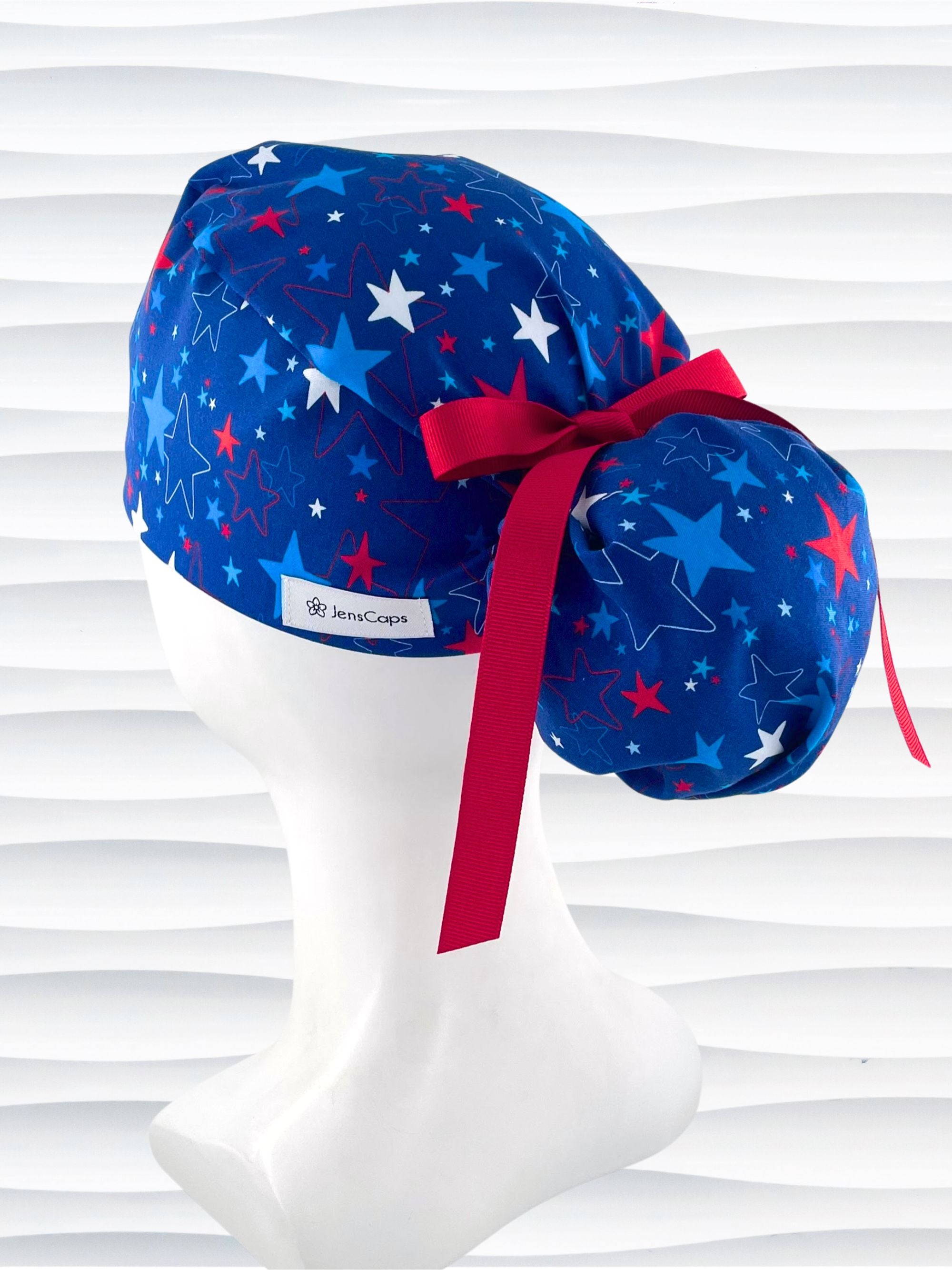 Ponytail style surgical scrub cap with an allover print of red white, and blue stars on royal blue cotton fabric.