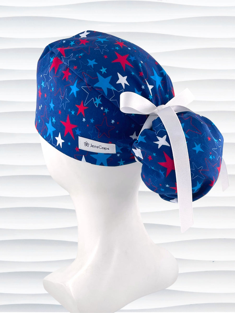 Ponytail style surgical scrub cap with an allover print of red white, and blue stars on royal blue cotton fabric.