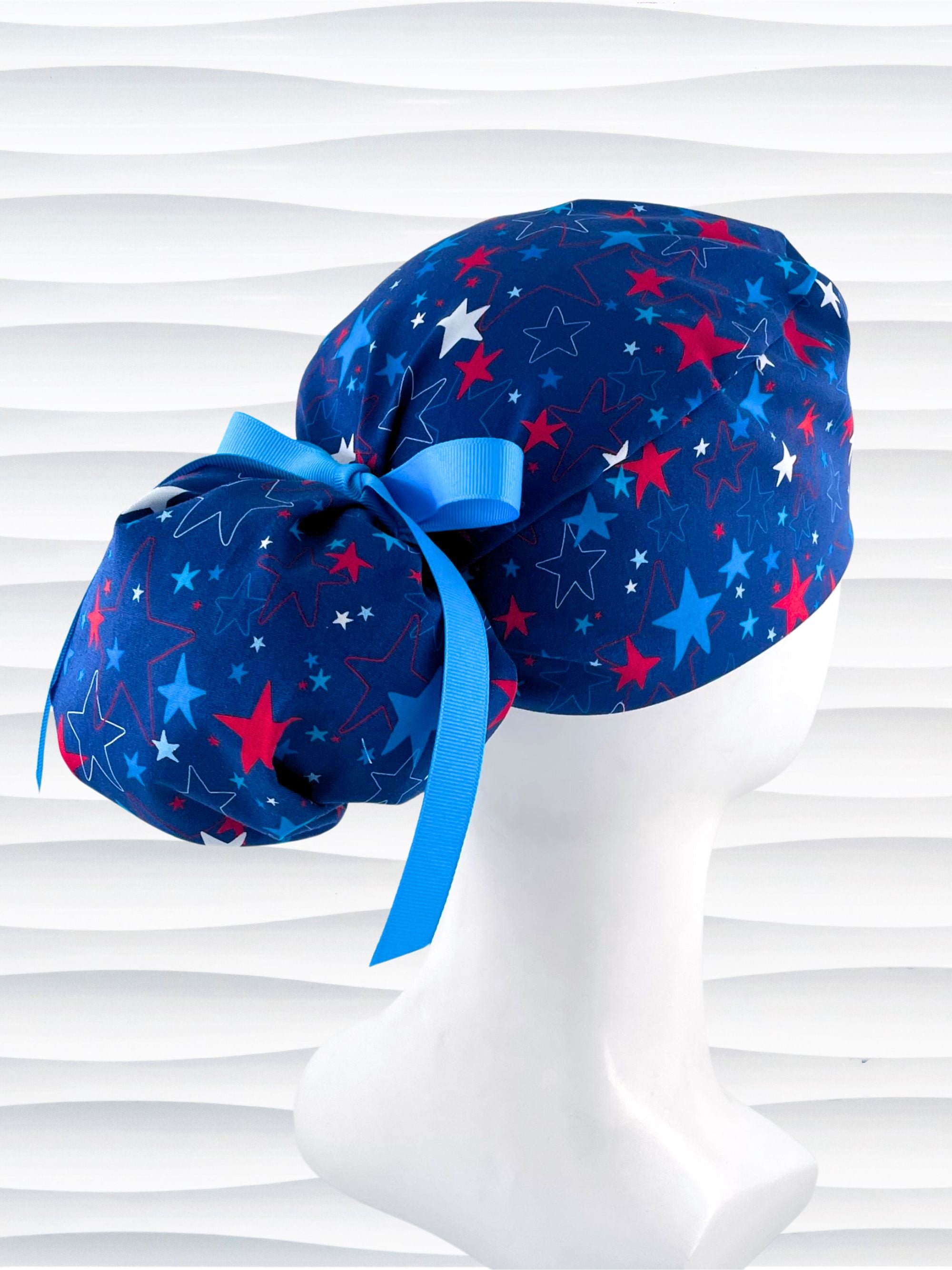 Ponytail style surgical scrub cap with an allover print of red white, and blue stars on royal blue cotton fabric.