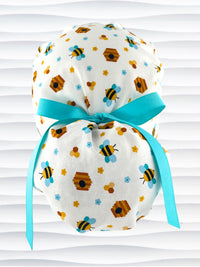 Ponytail style surgical scrub cap with honey bees with blue wings, blue and yellow daisies, and bee hives scattered all over this cotton fabric and tied with a grosgrain ribbon.