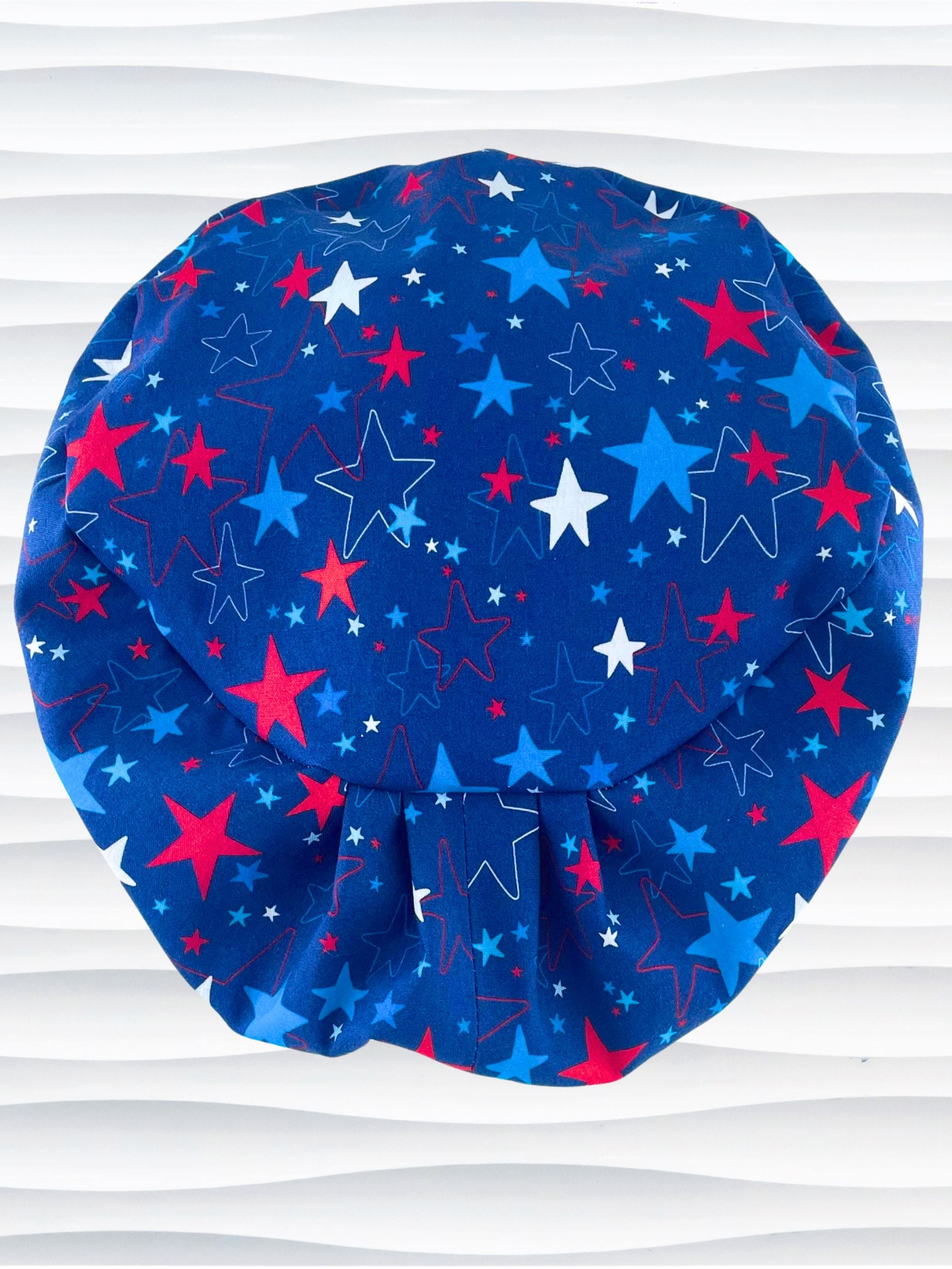 Euro Pixie style surgical scrub cap with an allover print of country style red white and blue stars on royal blue cotton fabric.