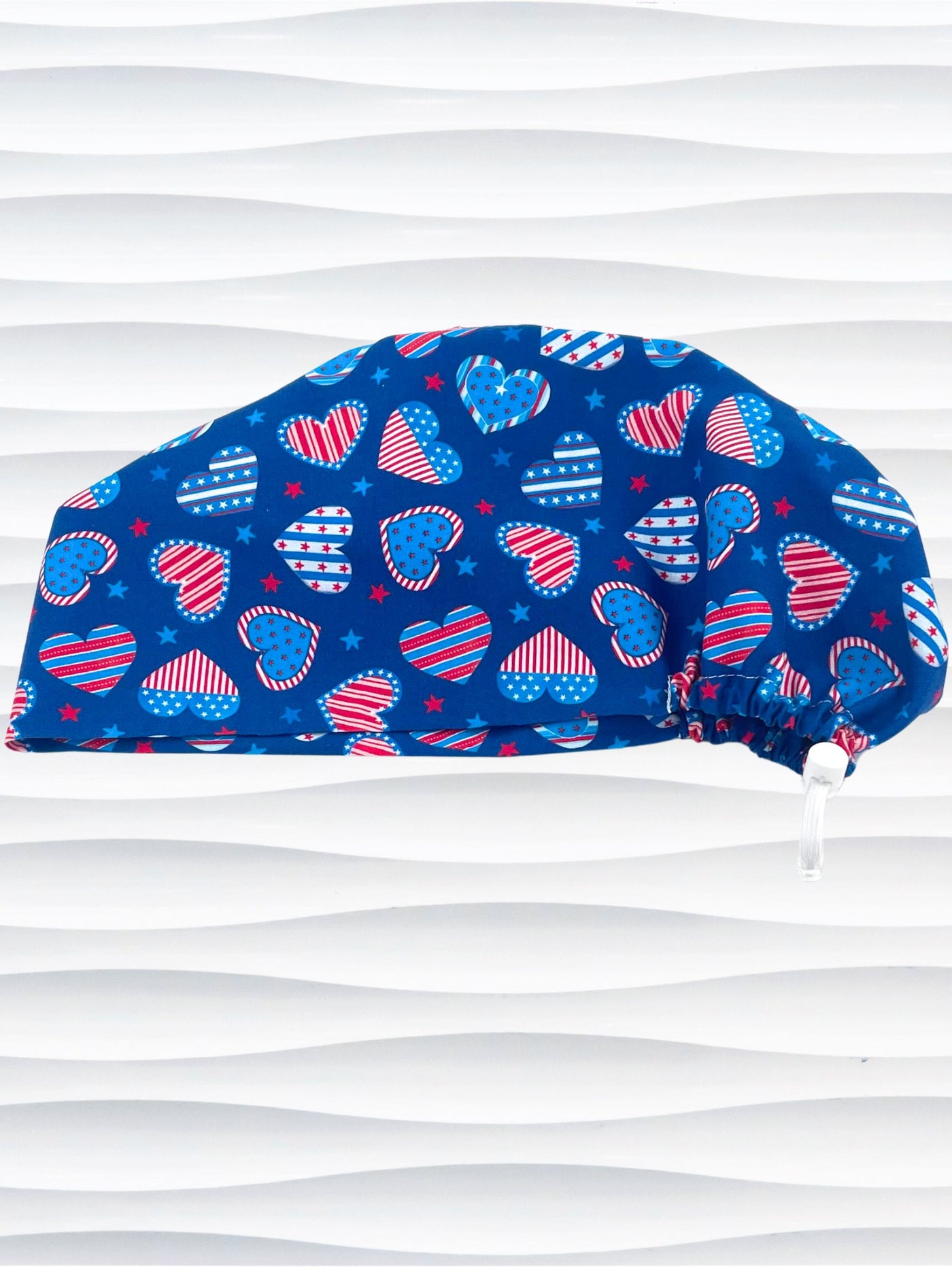 Euro Pixie style surgical scrub cap with an allover print of country style red white and blue hearts with dots, stars, and stripes on royal blue cotton fabric.