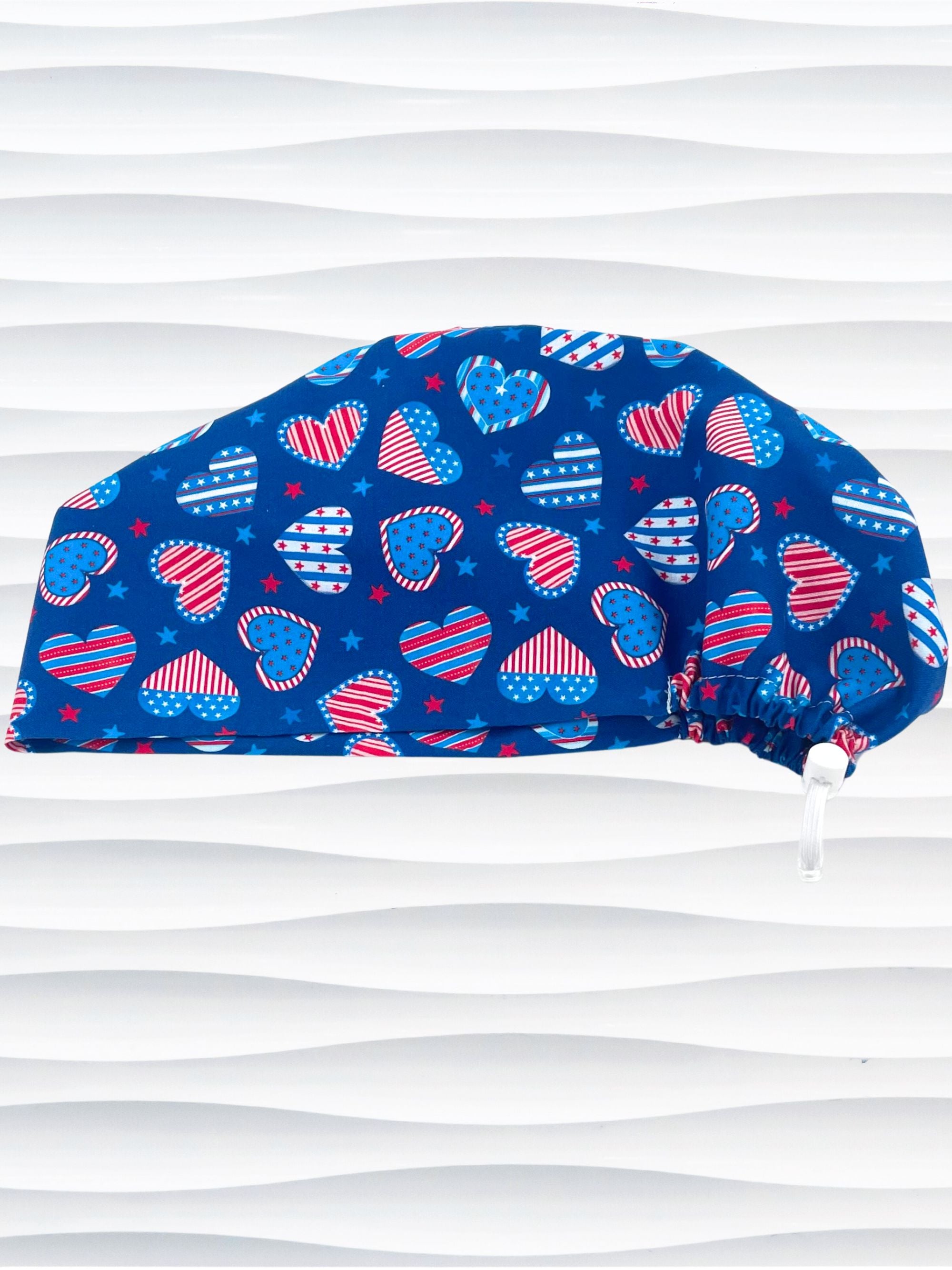 Euro Pixie style surgical scrub cap with an allover print of country style red white and blue hearts with dots, stars, and stripes on royal blue cotton fabric.