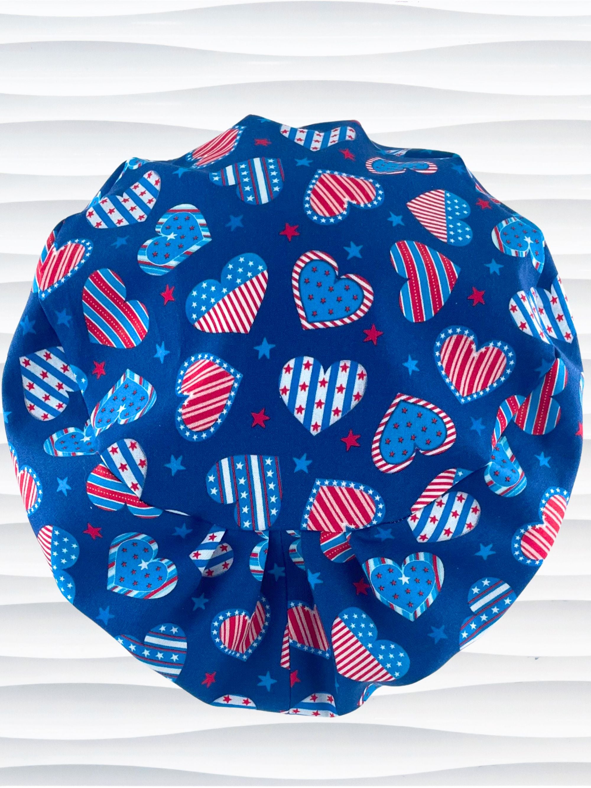 Euro Pixie style surgical scrub cap with an allover print of country style red white and blue hearts with dots, stars, and stripes on royal blue cotton fabric.