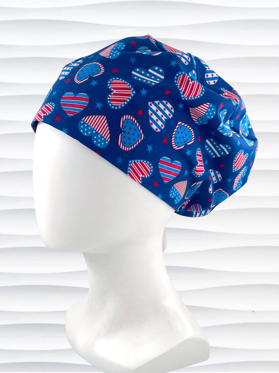 Euro Pixie style surgical scrub cap with an allover print of country style red white and blue hearts with dots, stars, and stripes on royal blue cotton fabric.