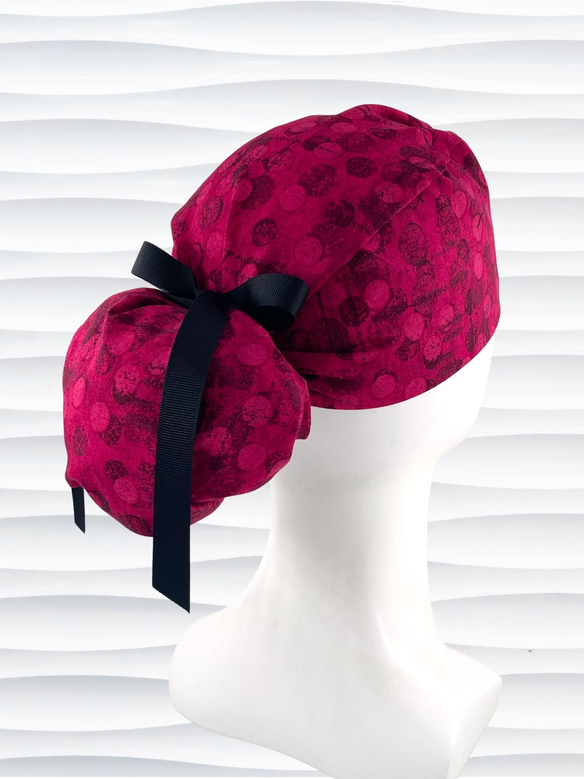 Ponytail pouch style surgical scrub cap with a muted pattern of black circles and lines on deep red or magenta cotton fabric.