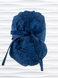 Ponytail pouch style surgical scrub cap with a muted pattern of flowers, ferns, and leaves in dark blue on a deep royal blue cotton fabric.