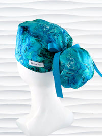 Ponytail pouch style surgical scrub cap with a marbled pattern of blues and green that look like ocean tide pools or marbled turquoise on cotton fabric.