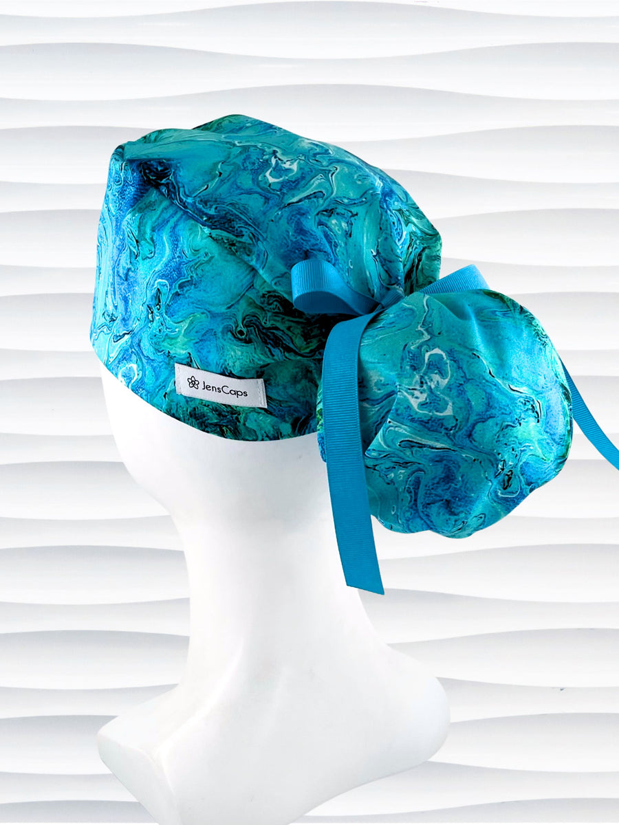 Ponytail pouch style surgical scrub cap with a marbled pattern of blues and green that look like ocean tide pools or marbled turquoise on cotton fabric.