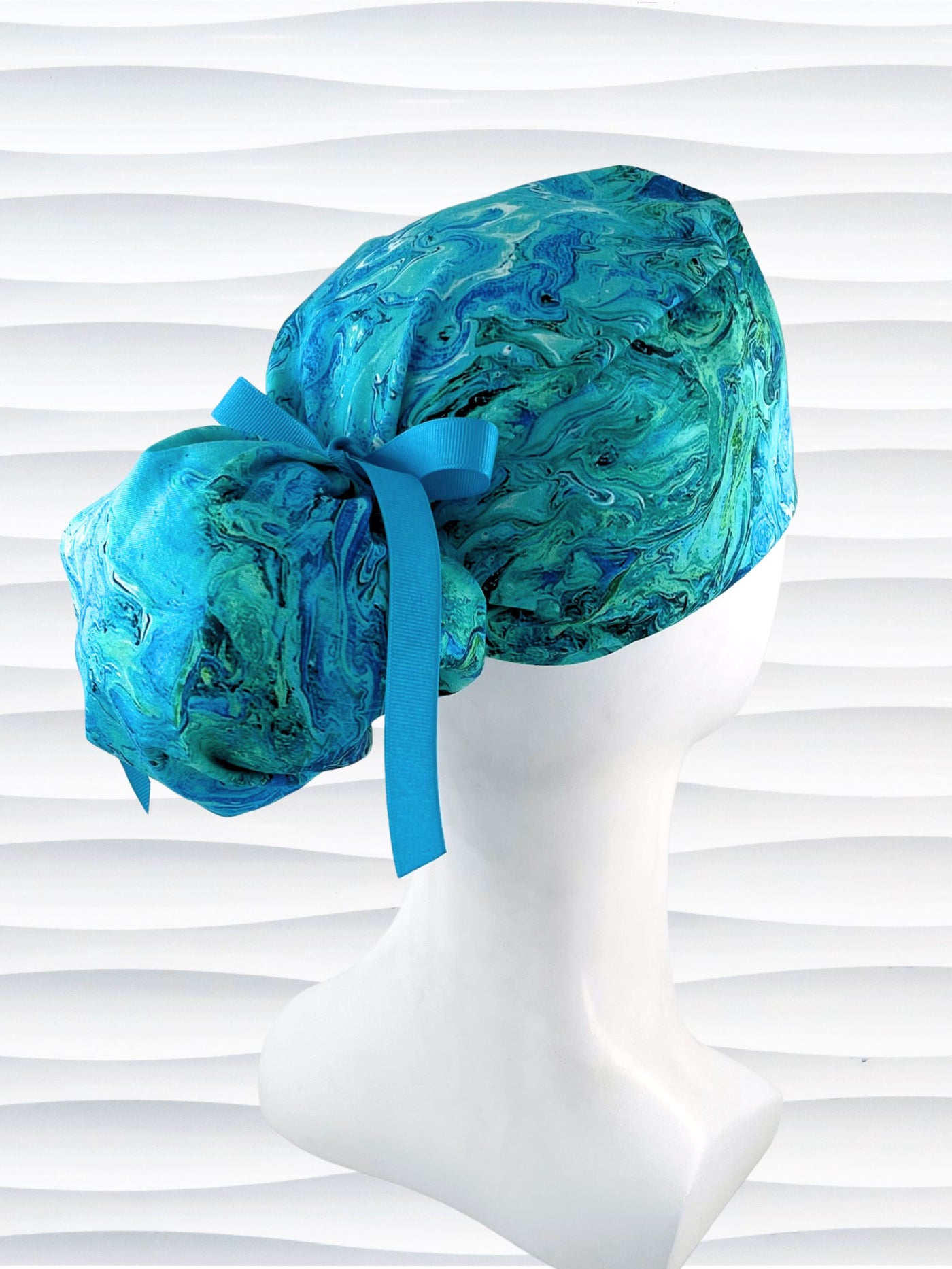 Ponytail pouch style surgical scrub cap with a marbled pattern of blues and green that look like ocean tide pools or marbled turquoise on cotton fabric.
