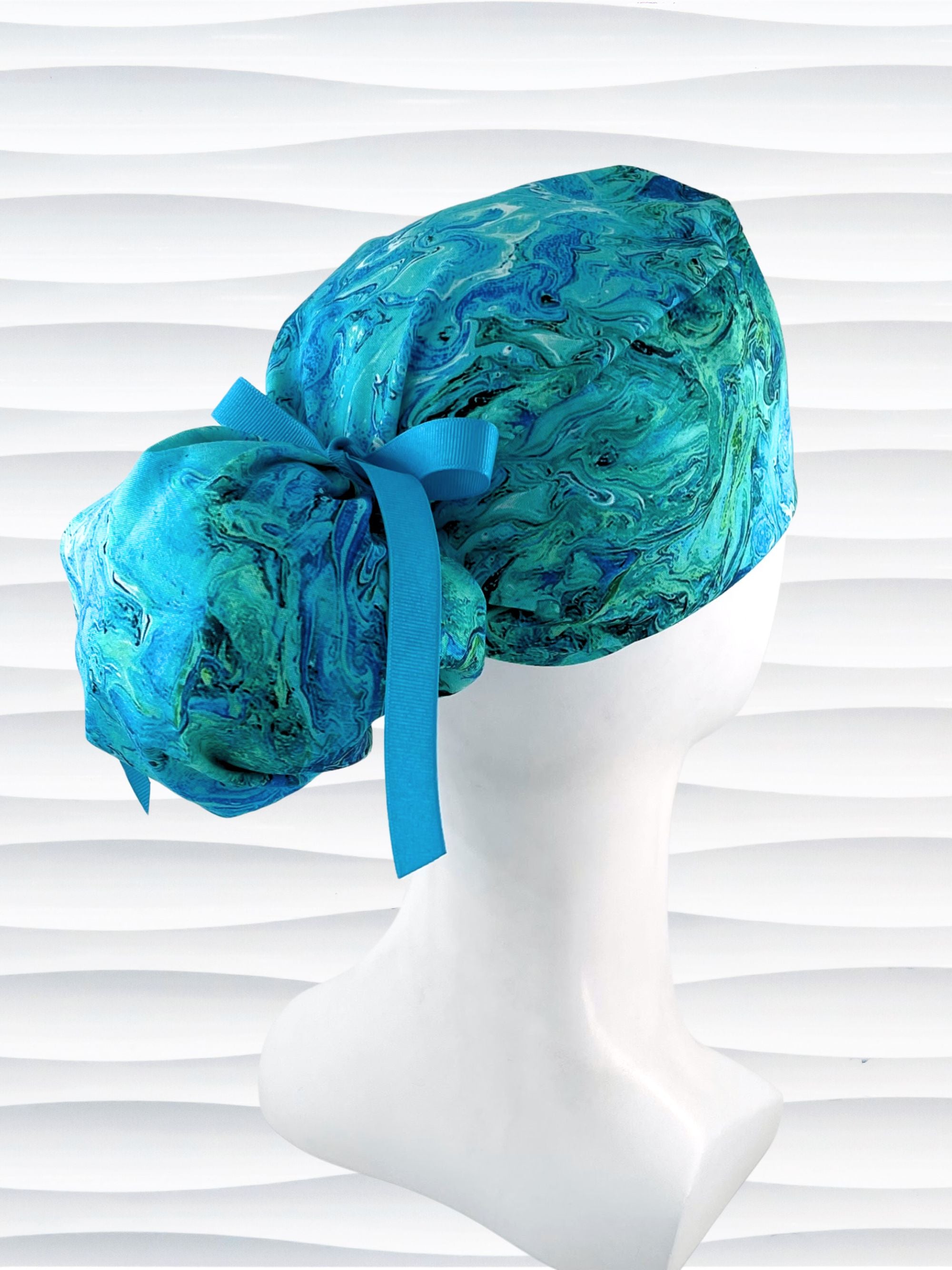 Ponytail pouch style surgical scrub cap with a marbled pattern of blues and green that look like ocean tide pools or marbled turquoise on cotton fabric.