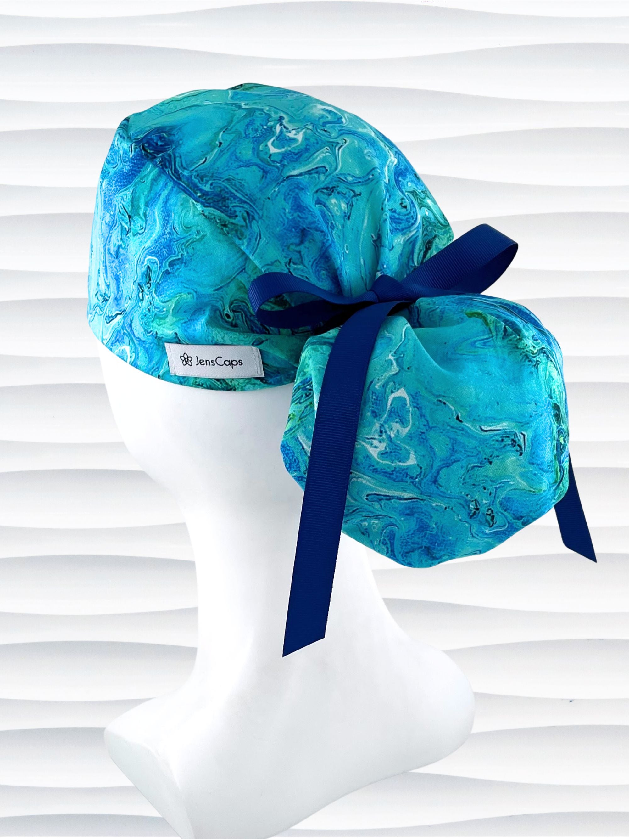 Ponytail pouch style surgical scrub cap with a marbled pattern of blues and green that look like ocean tide pools or marbled turquoise on cotton fabric.