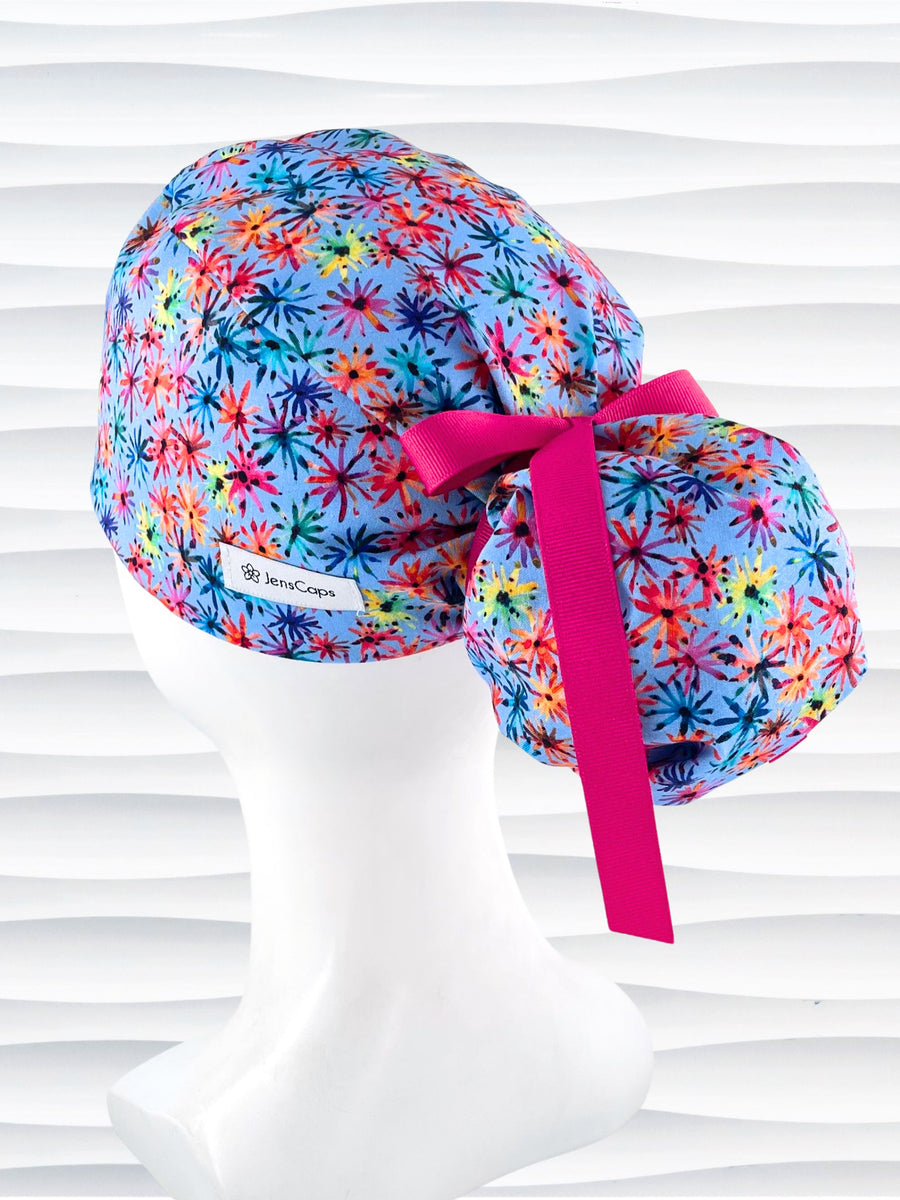 Ponytail pouch style surgical scrub cap with floral fireworks in pinks, reds, blues, yellow, and purple on cotton fabric and finished with a grosgrain ribbon tie.