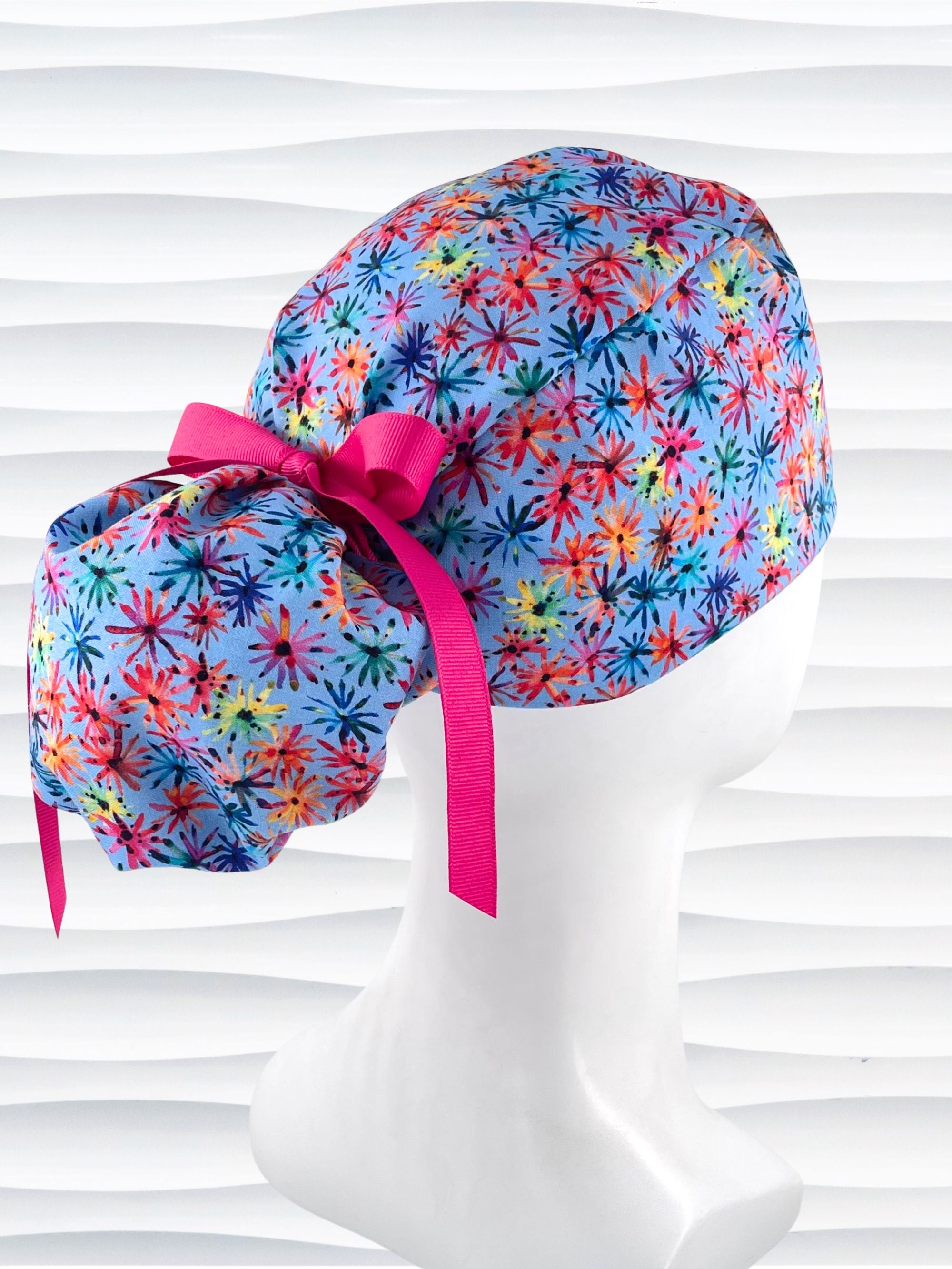 Ponytail pouch style surgical scrub cap with floral fireworks in pinks, reds, blues, yellow, and purple on cotton fabric and finished with a grosgrain ribbon tie.