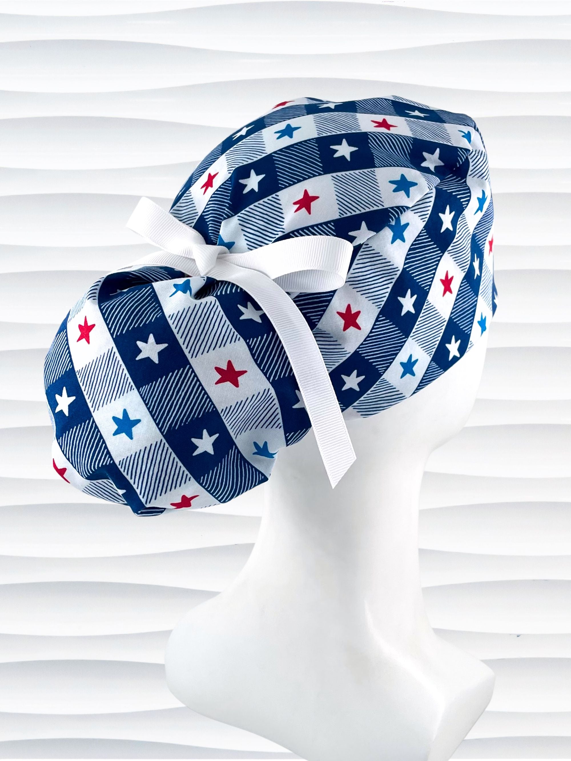 Ponytail pouch style surgical scrub cap with a fun plaid print in blue and white with red, white, and blue stars on cotton fabric.
