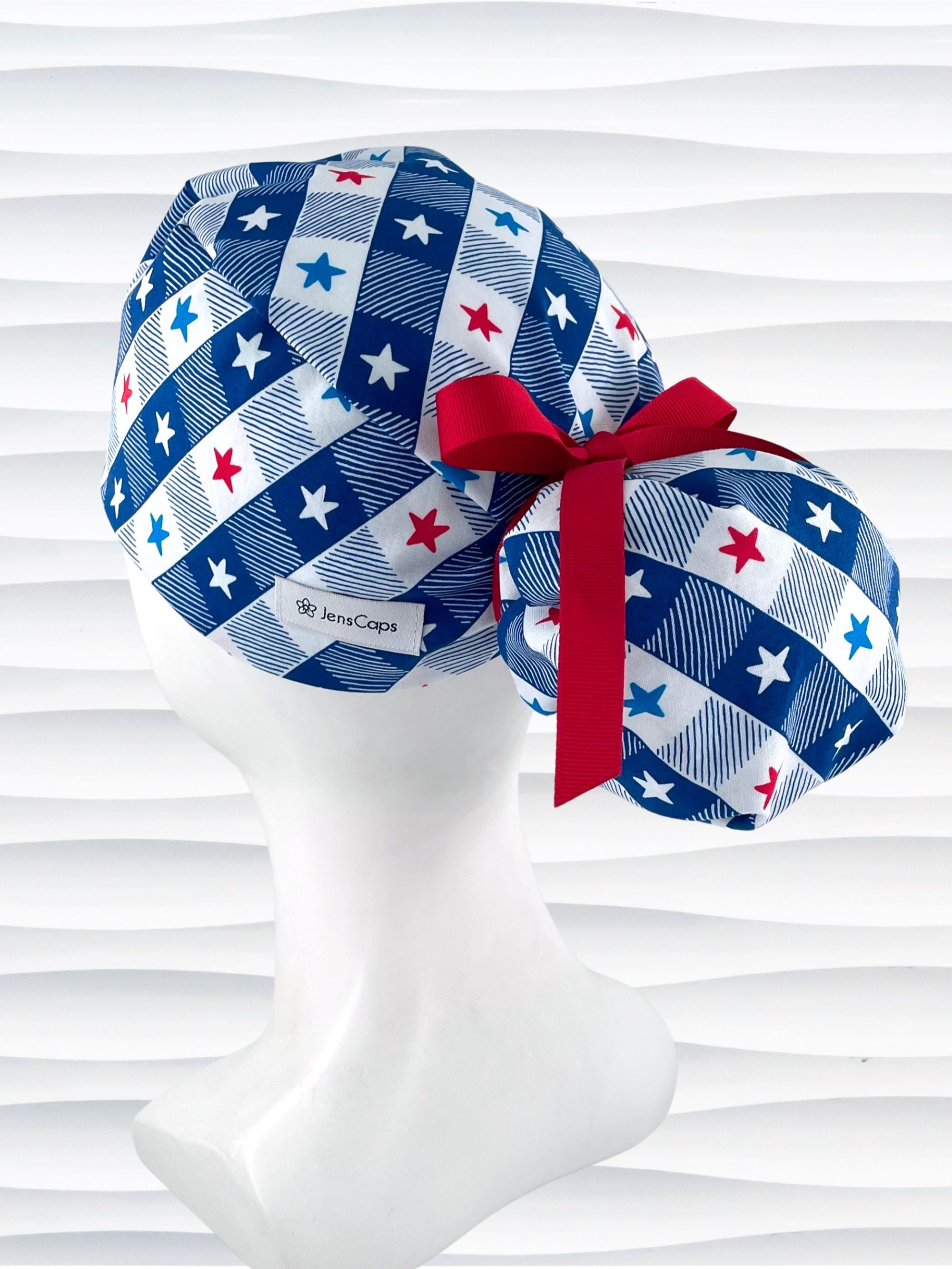 Ponytail pouch style surgical scrub cap with a fun plaid print in blue and white with red, white, and blue stars on cotton fabric.