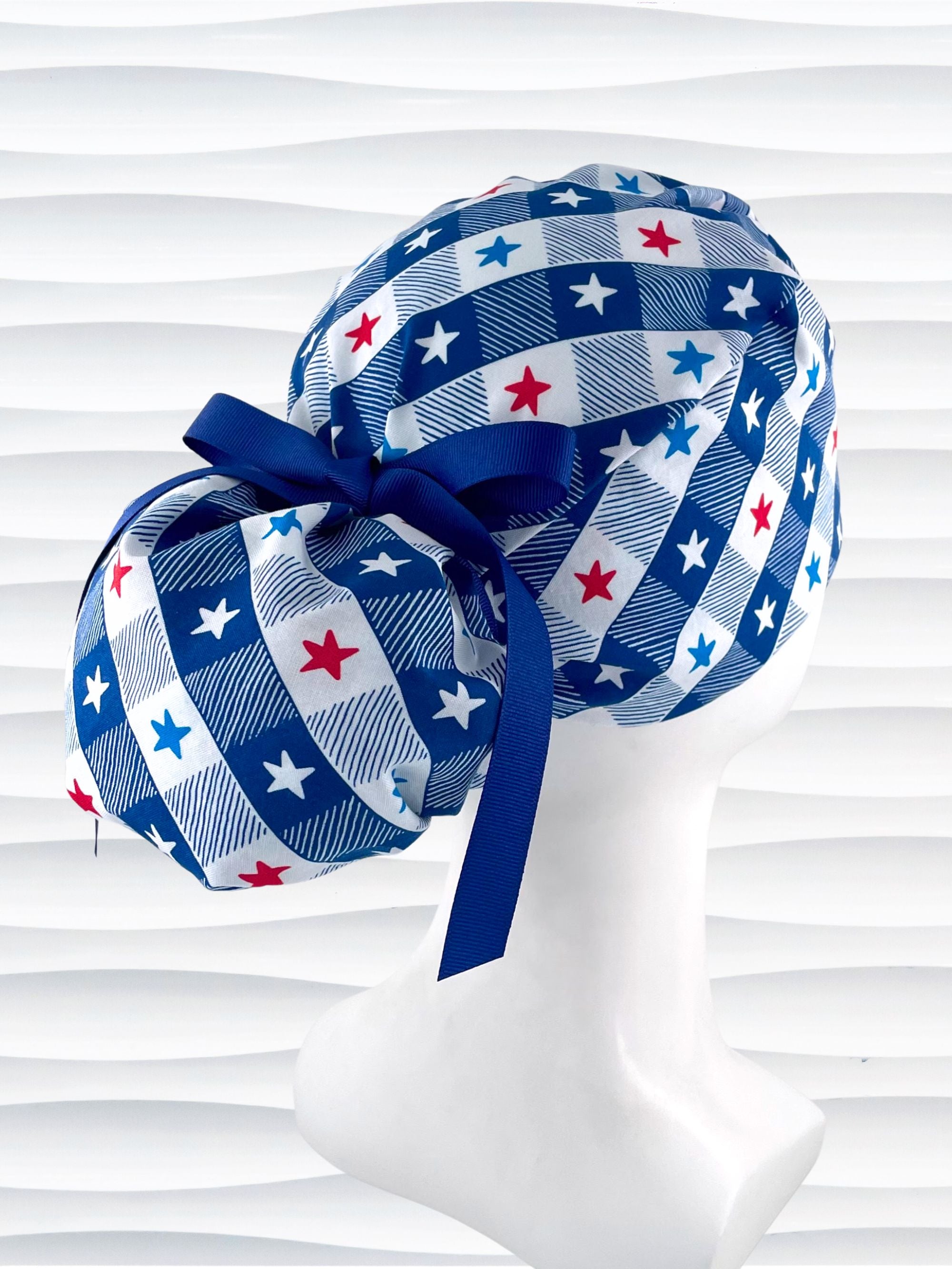 Ponytail pouch style surgical scrub cap with a fun plaid print in blue and white with red, white, and blue stars on cotton fabric.
