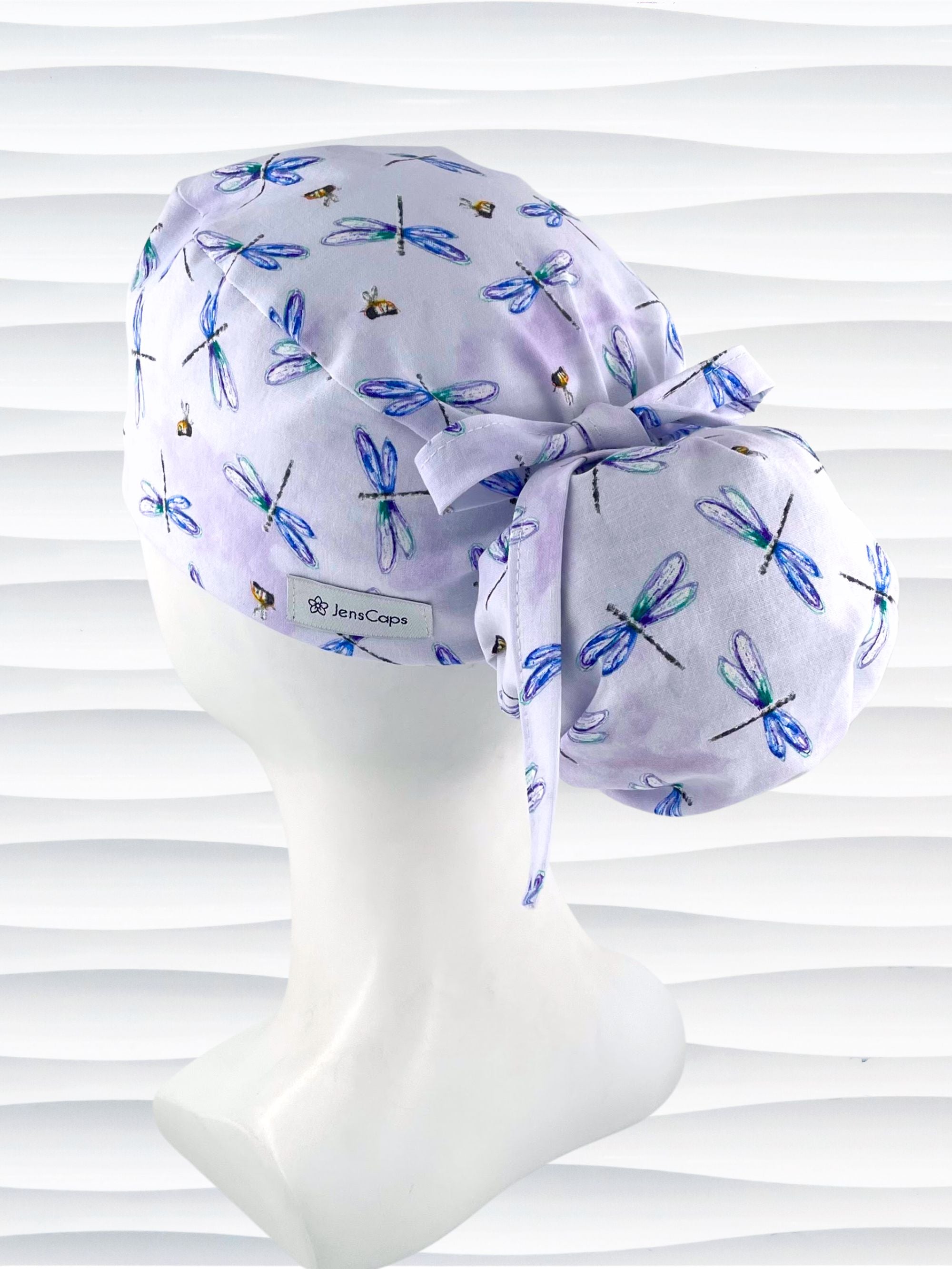 Ponytail pouch style surgical scrub cap hat with blue and purple dragonflies and honey bees all over lavender background cotton fabric.