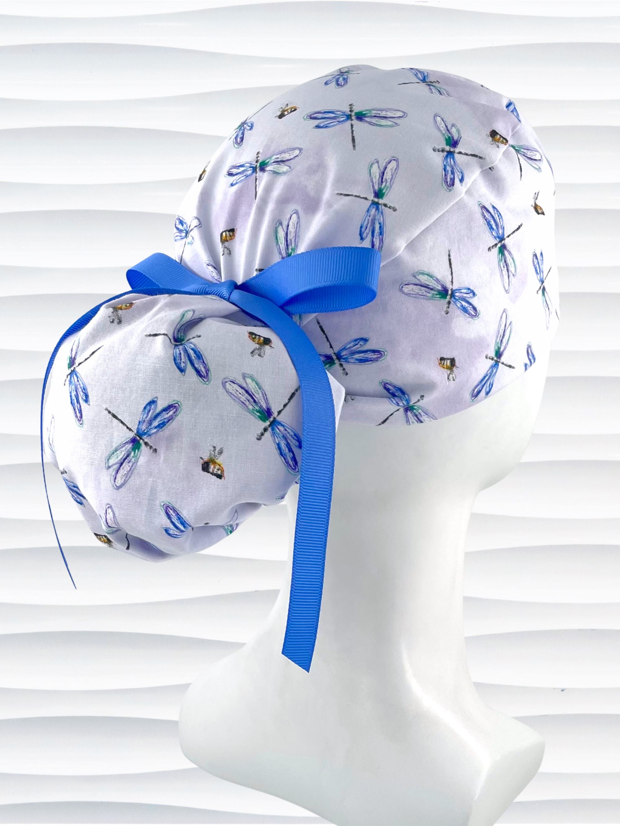 Ponytail pouch style surgical scrub cap hat with blue and purple dragonflies and honey bees all over lavender background cotton fabric.