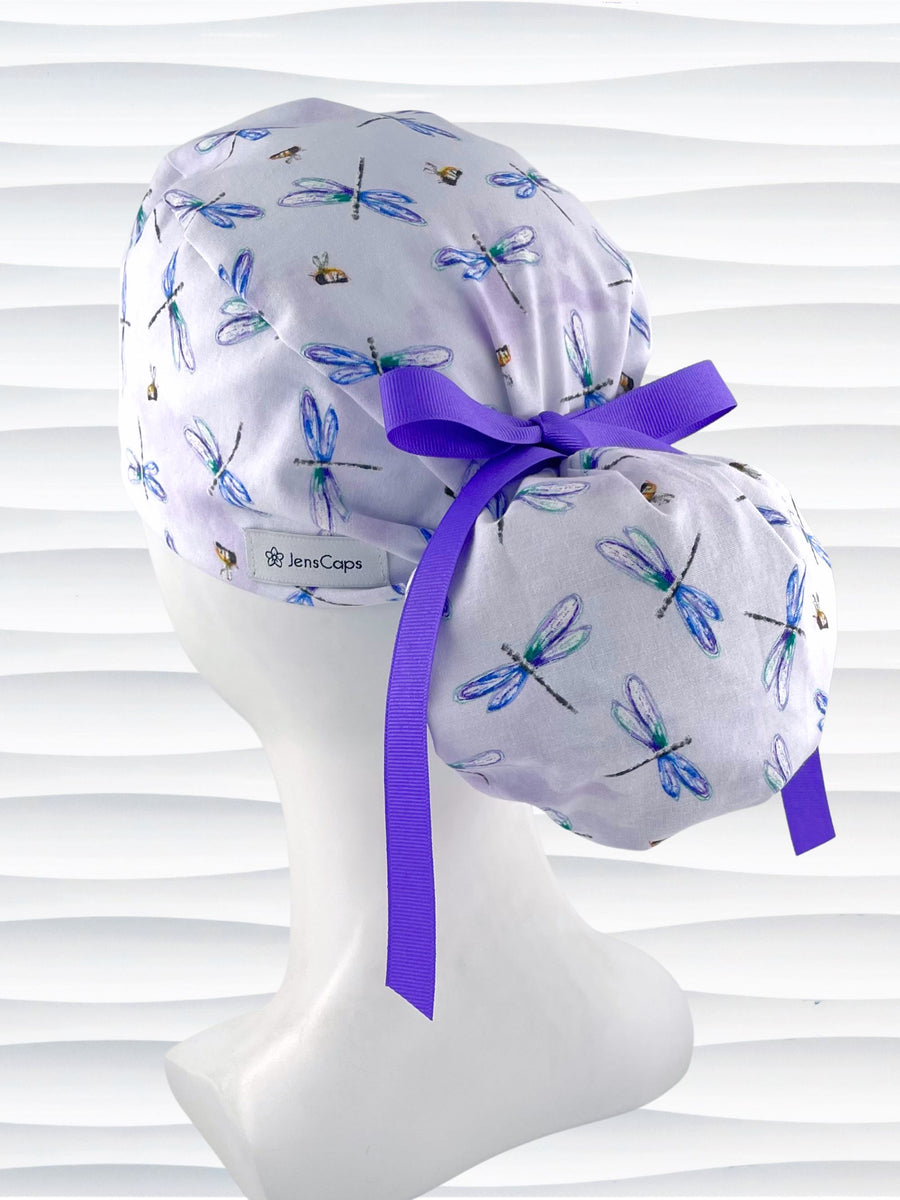 Ponytail pouch style surgical scrub cap hat with blue and purple dragonflies and honey bees all over lavender background cotton fabric.