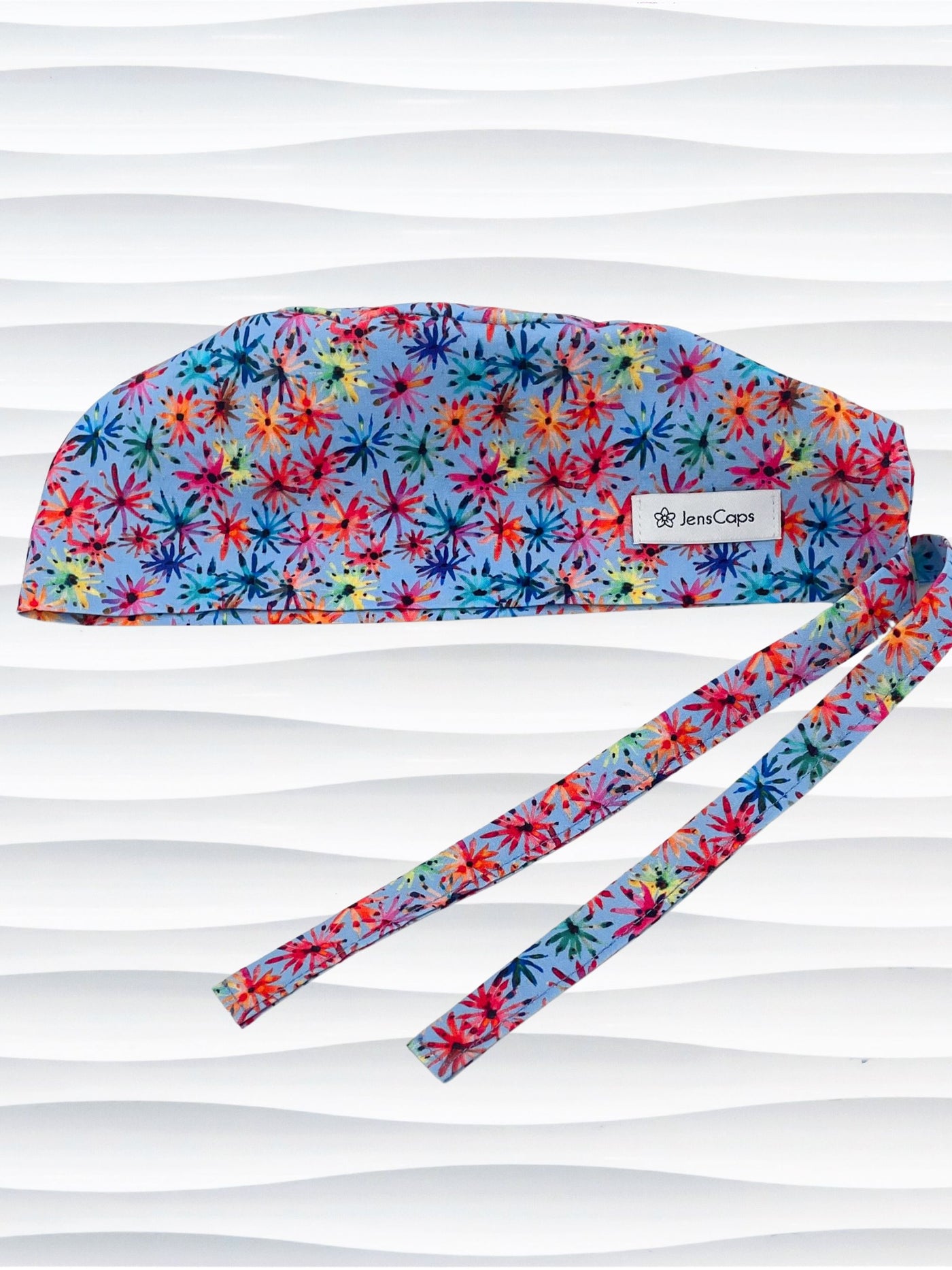 Surgeon style surgical scrub cap by JensCaps with red, blue, yellow, and green fireworks that look like flowers all over a medium blue background on cotton fabric.