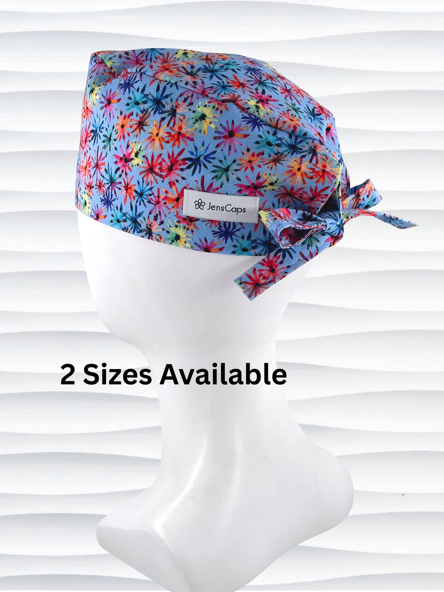 Surgeon style surgical scrub cap by JensCaps with red, blue, yellow, and green fireworks that look like flowers all over a medium blue background on cotton fabric.