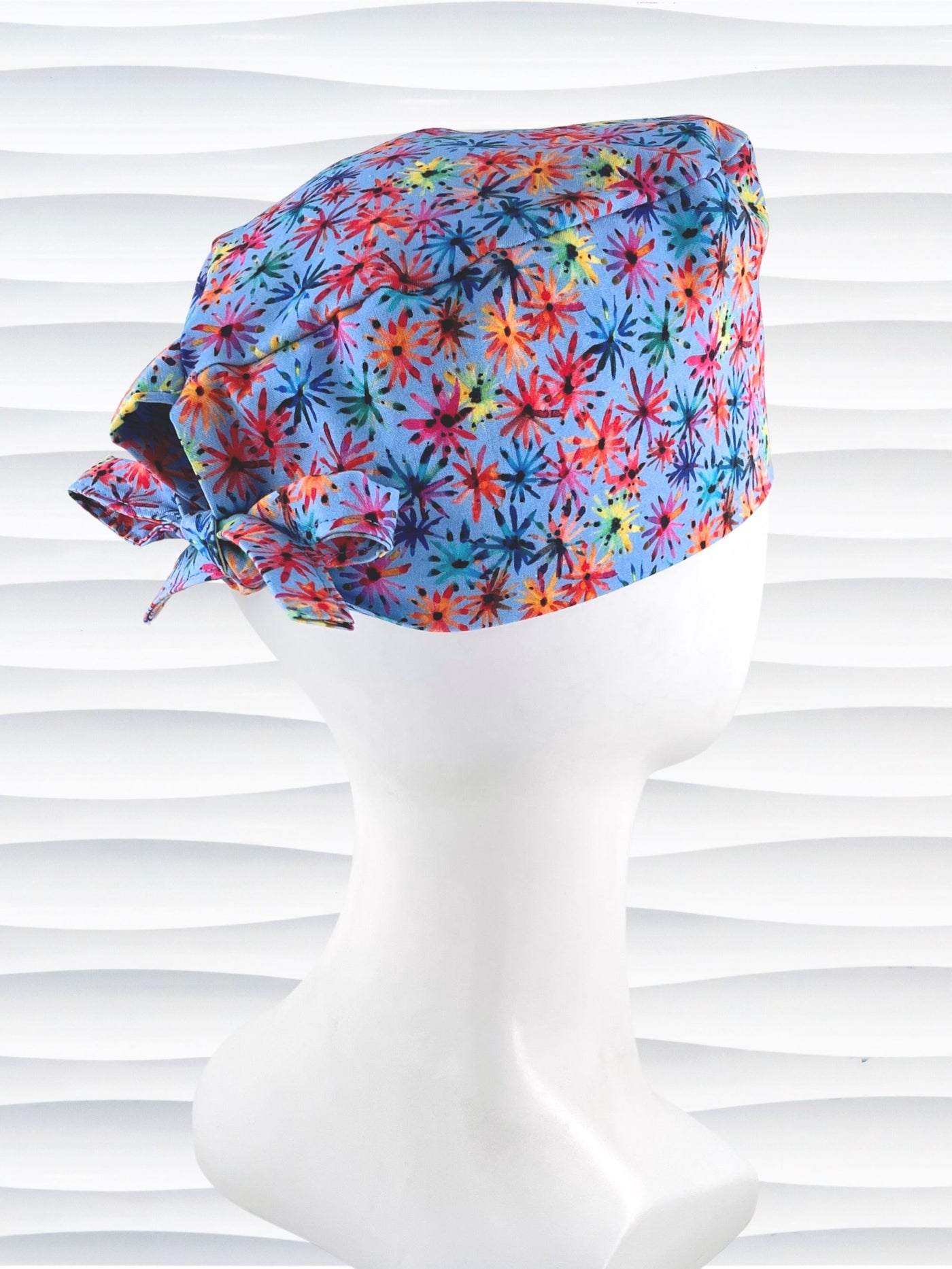 Surgeon style surgical scrub cap by JensCaps with red, blue, yellow, and green fireworks that look like flowers all over a medium blue background on cotton fabric.