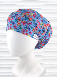 Bouffant style surgical scrub cap with bright flowers that look like fireworks in red, pink, yellow, blue, and green all over blue cotton fabric.