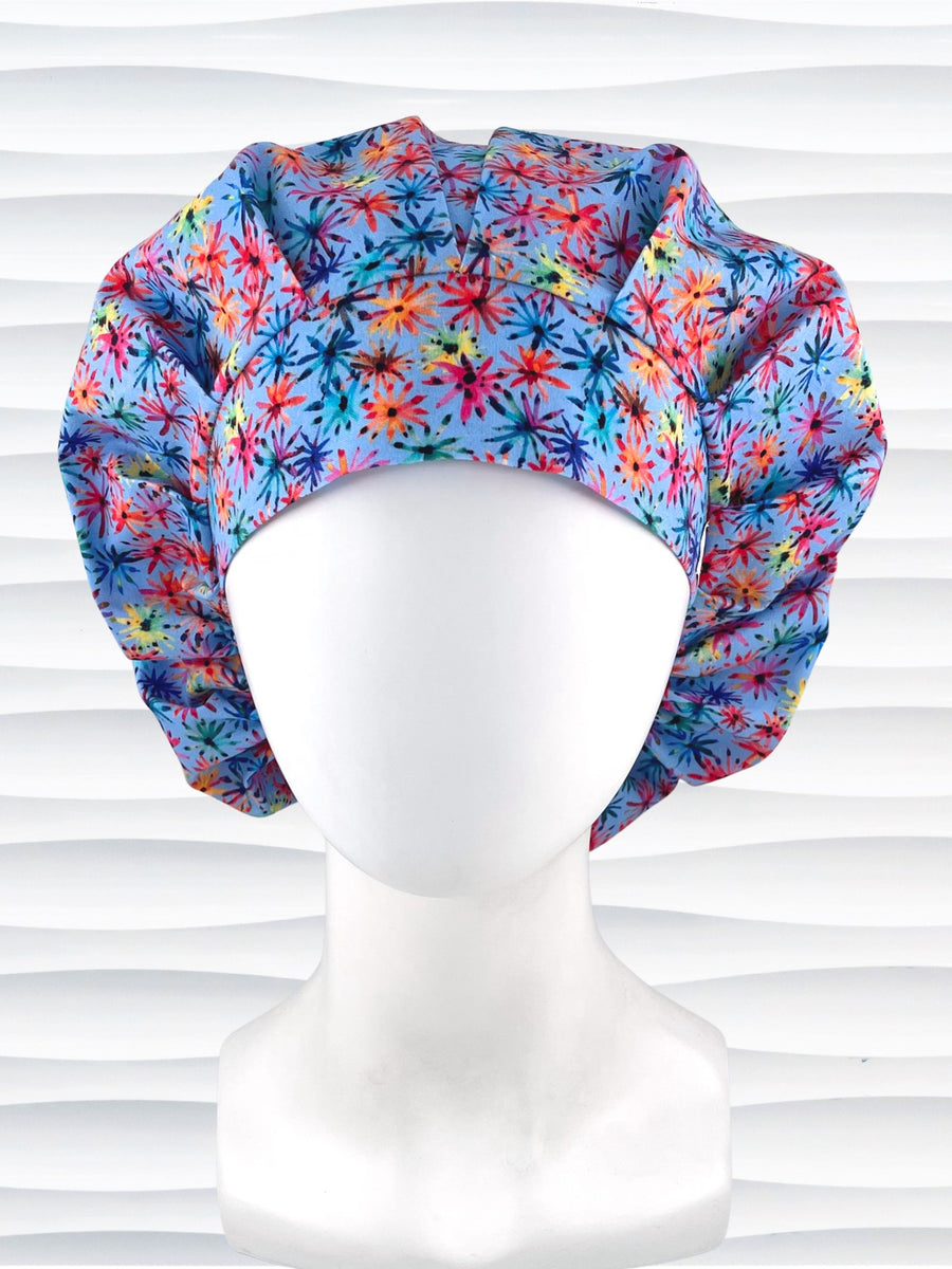 Bouffant style surgical scrub cap with bright flowers that look like fireworks in red, pink, yellow, blue, and green all over blue cotton fabric.