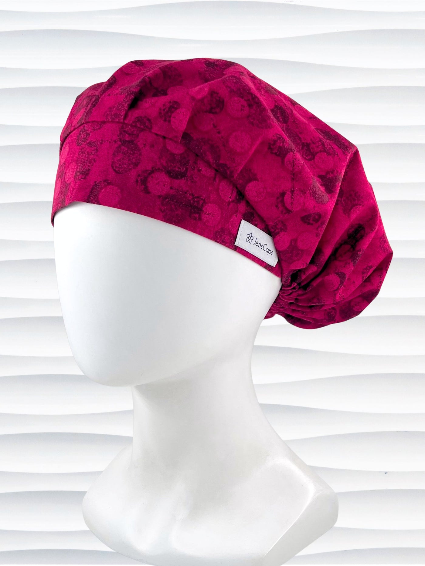 Bouffant style surgical scrub cap with a muted pattern of black circles and lines on deep red or magenta cotton fabric.