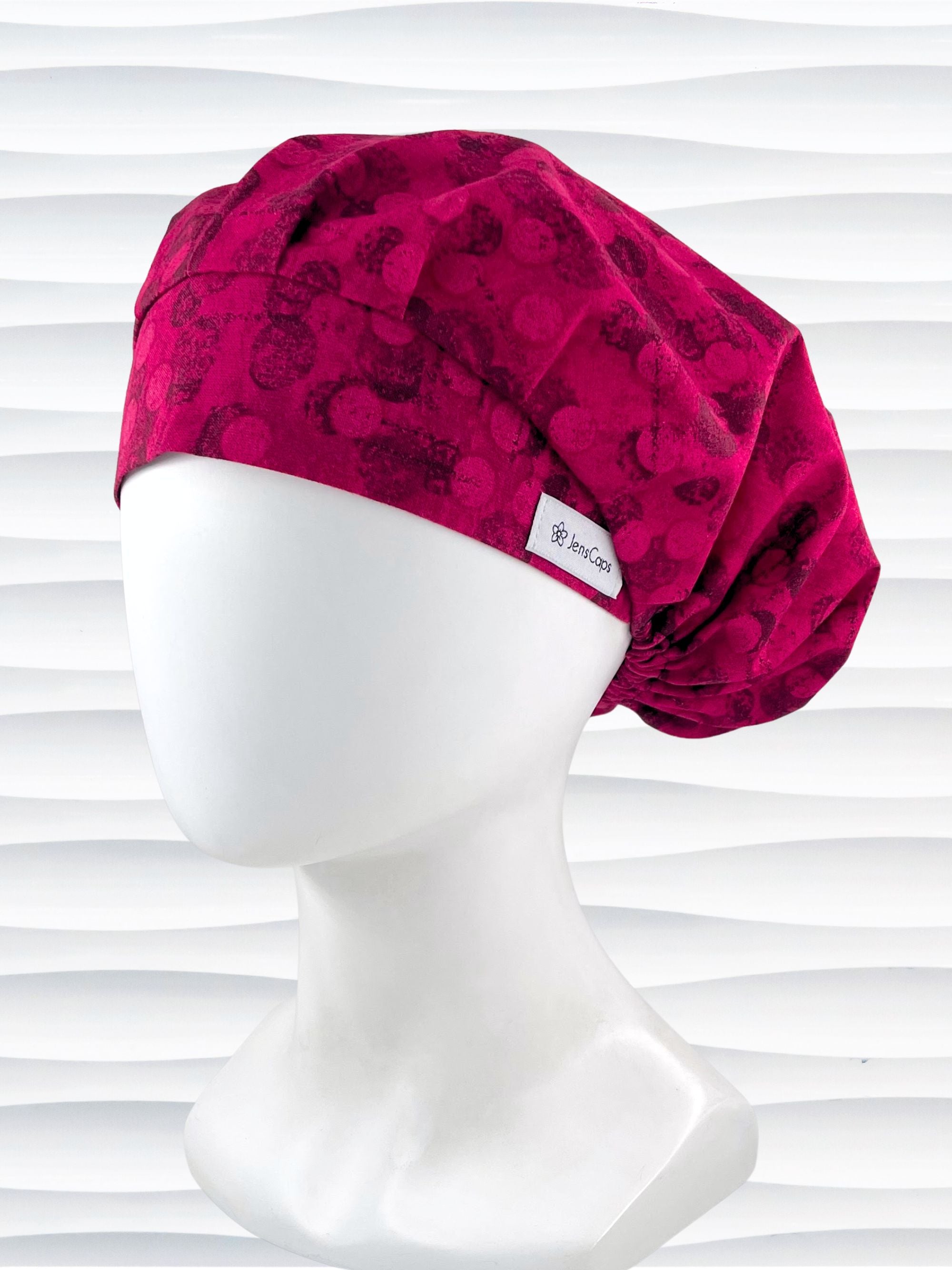 Bouffant style surgical scrub cap with a muted pattern of black circles and lines on deep red or magenta cotton fabric.