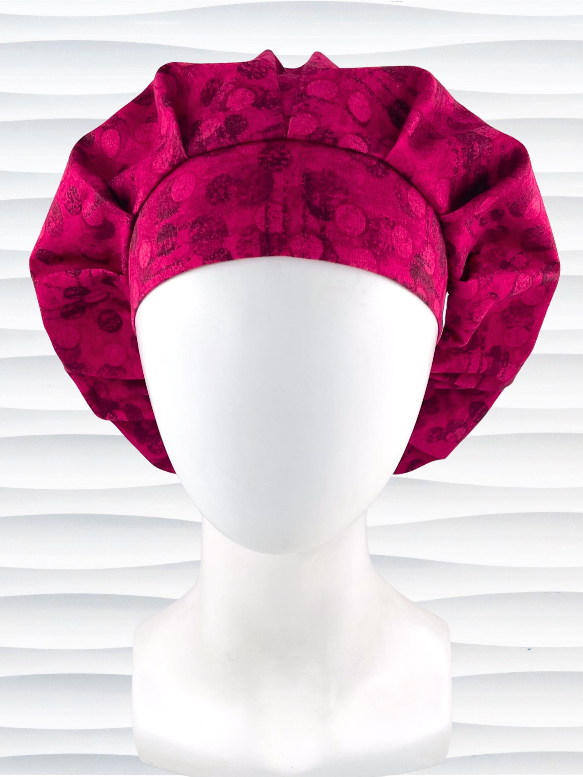 Bouffant style surgical scrub cap with a muted pattern of black circles and lines on deep red or magenta cotton fabric.
