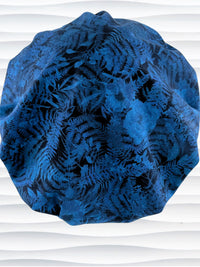 Bouffant style surgical scrub cap with a muted pattern of flowers, ferns, and leaves in dark blue on a deep royal blue cotton fabric.