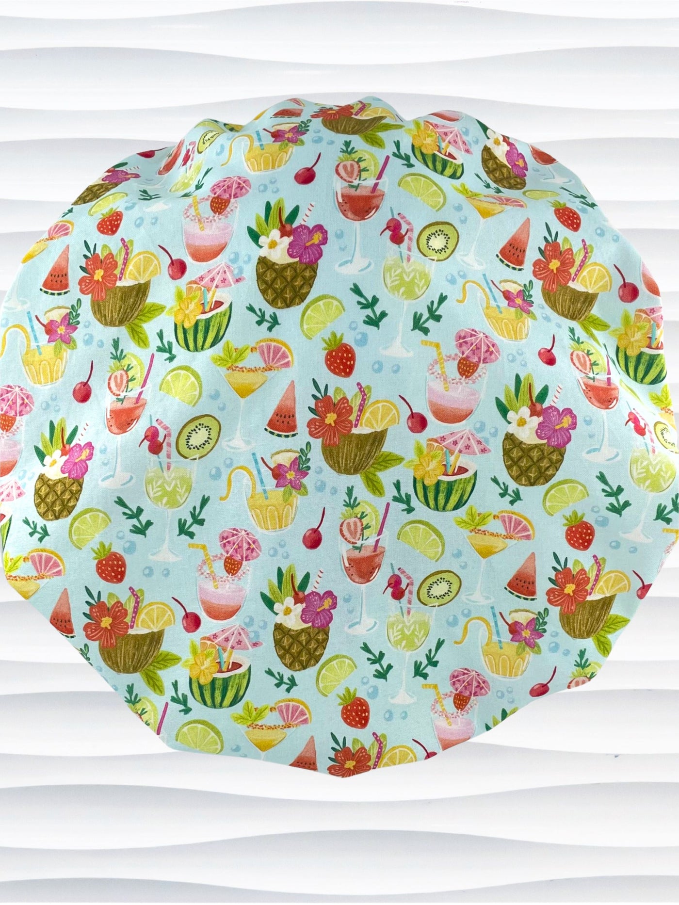 Bouffant surgical scrub cap by JensCaps with iconic tropical drinks with umbrellas and flowers in pinks and yellows and greens on light blue cotton fabric.
