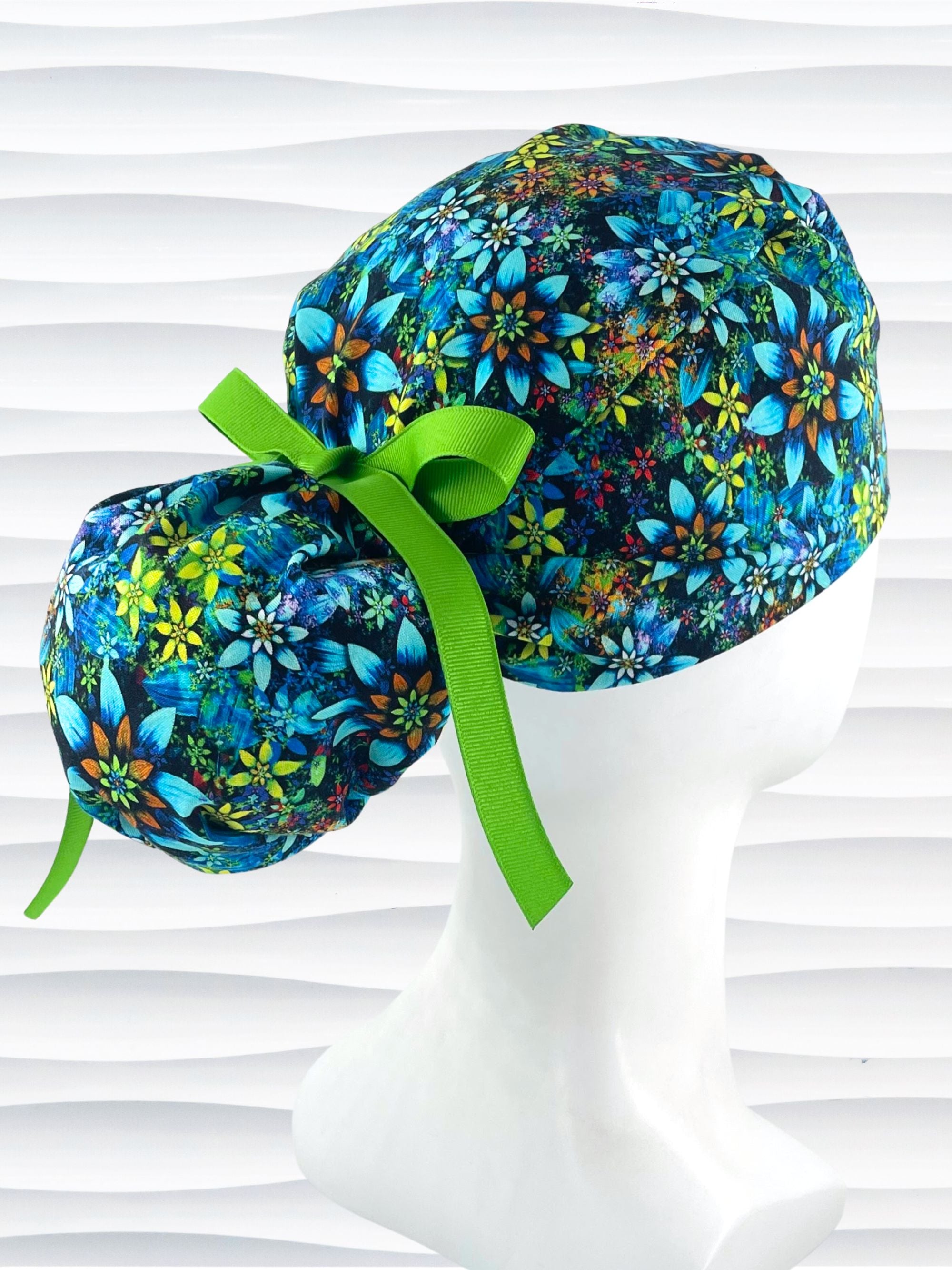 Ponytail style surgical scrub cap with bright yellow, orange, white, and blue flowers with dark blue background on cotton fabric.