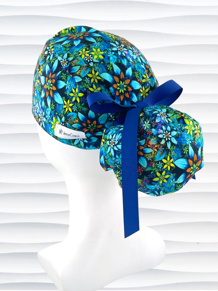 Ponytail style surgical scrub cap with bright yellow, orange, white, and blue flowers with dark blue background on cotton fabric.