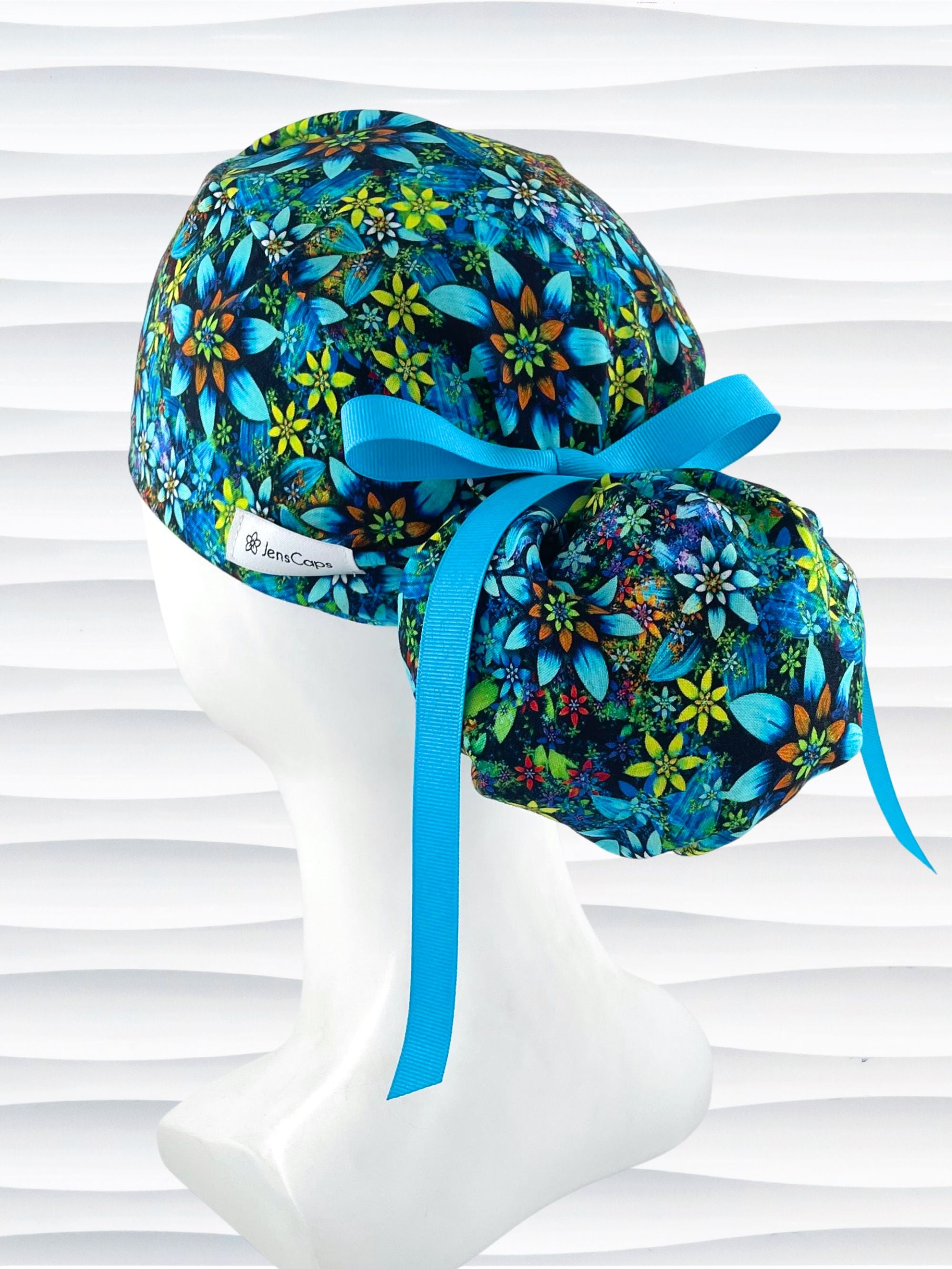 Ponytail style surgical scrub cap with bright yellow, orange, white, and blue flowers with dark blue background on cotton fabric.