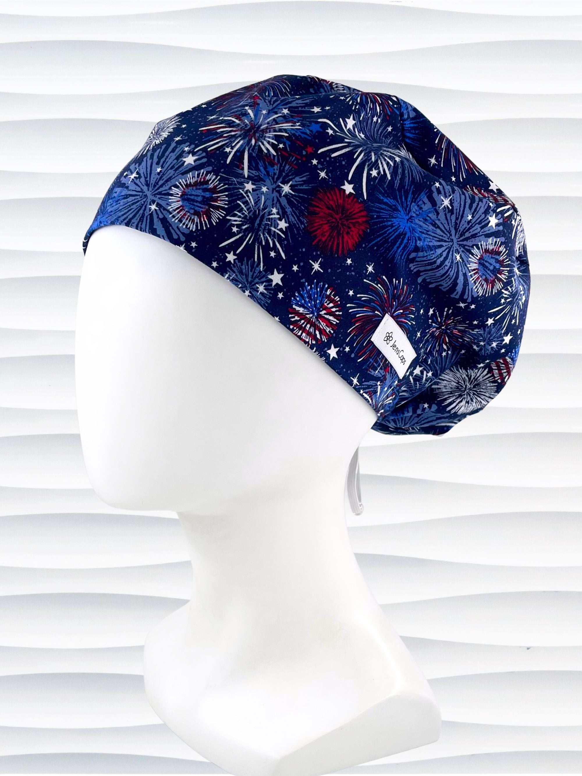 Euro Pixie style surgical scrub cap by JensCaps with fireworks and stars in red white and blue all over navy blue cotton fabric.