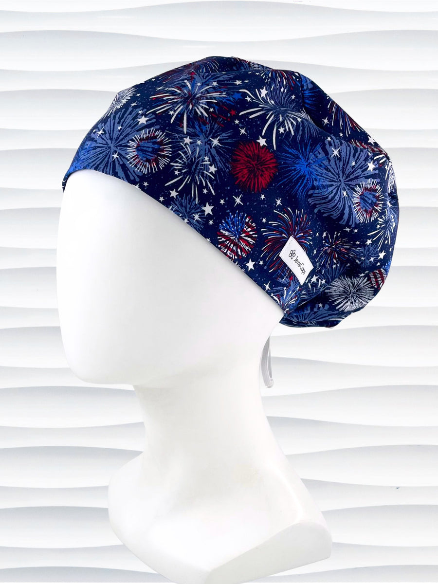 Euro Pixie style surgical scrub cap by JensCaps with fireworks and stars in red white and blue all over navy blue cotton fabric.