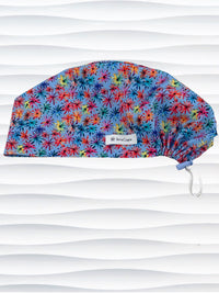 Euro Pixie style surgical scrub cap with bright flowers that look like fireworks in red, pink, yellow, blue, and green all over blue cotton fabric.