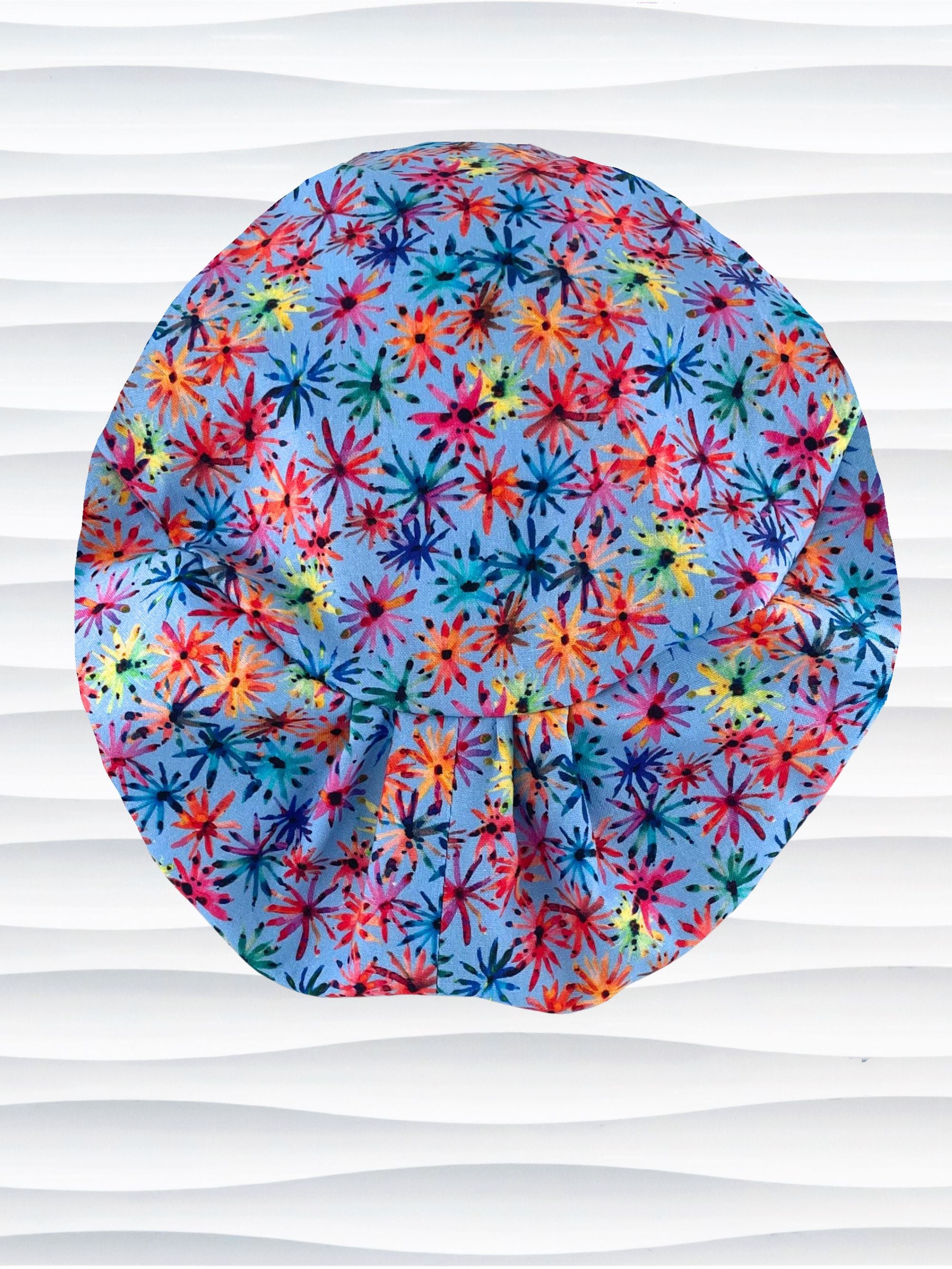 Euro Pixie style surgical scrub cap with bright flowers that look like fireworks in red, pink, yellow, blue, and green all over blue cotton fabric.