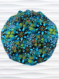 Bouffant style surgical scrub cap with electric bright flowers in green, yellow, white, orange, and blue all over a dark background cotton fabric.